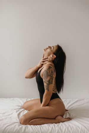 Nainen polvillaan sängyllä, itsevarma ja voimakas boudoir-poseeraus