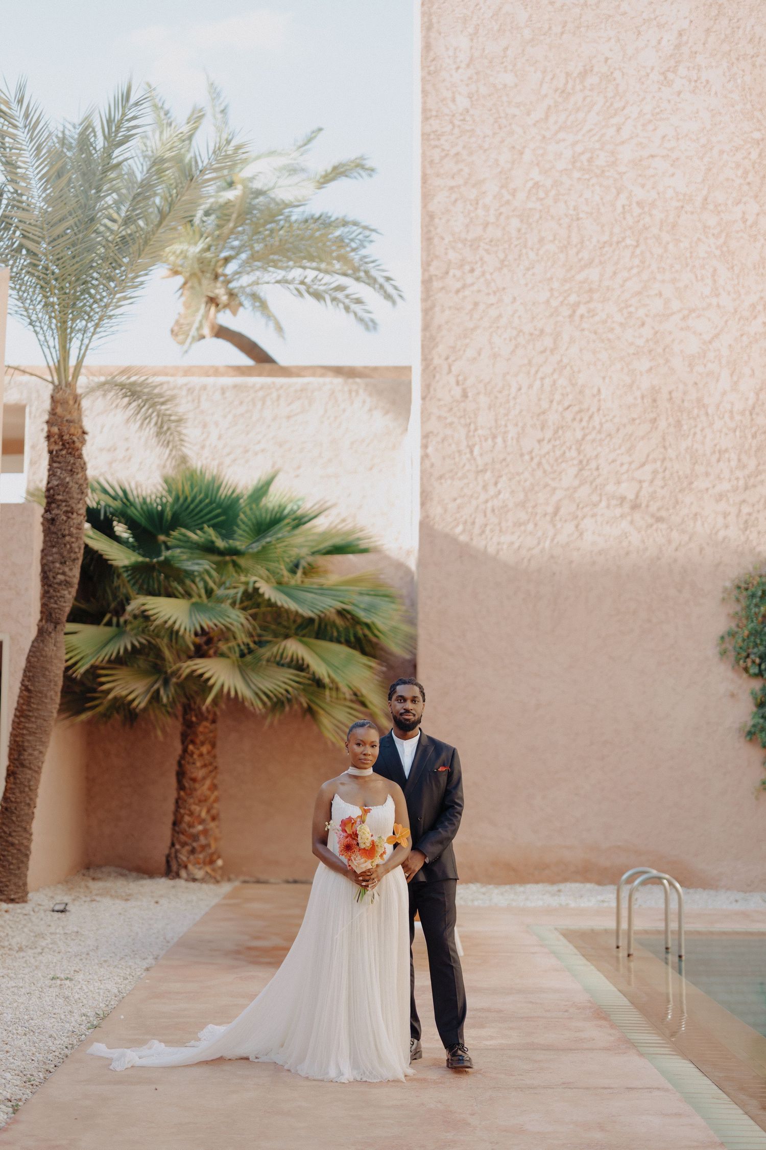 A wedding couple walking and laughing together on a tree-lined path in formal attire.