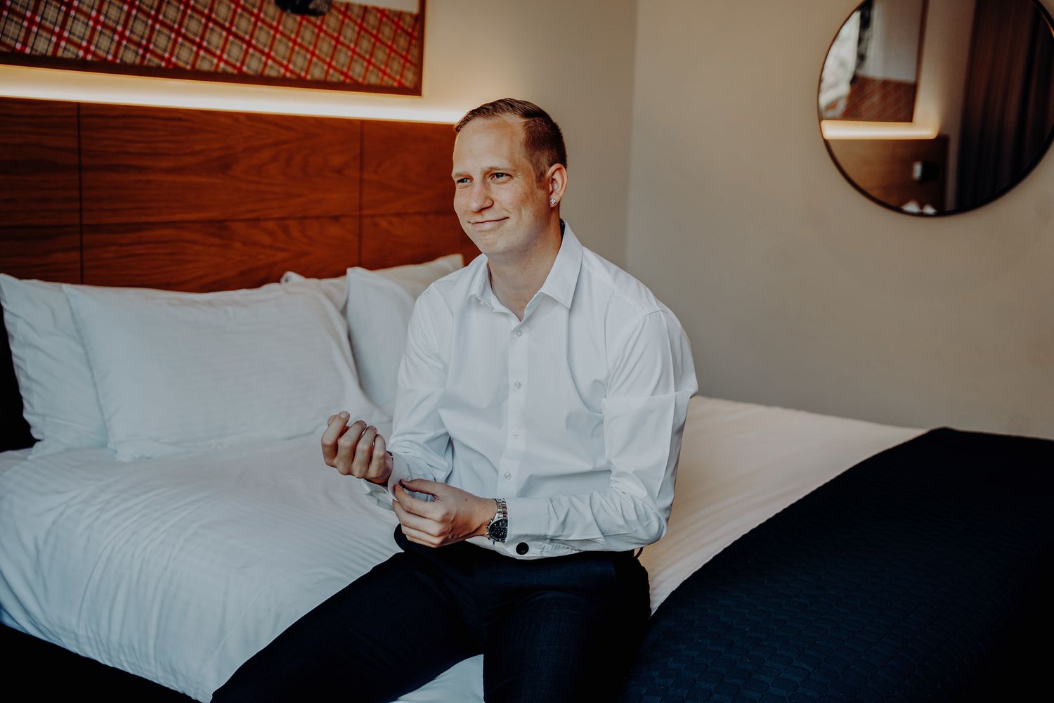 Someone in a white dress shirt sits on a hotel bed while getting ready.