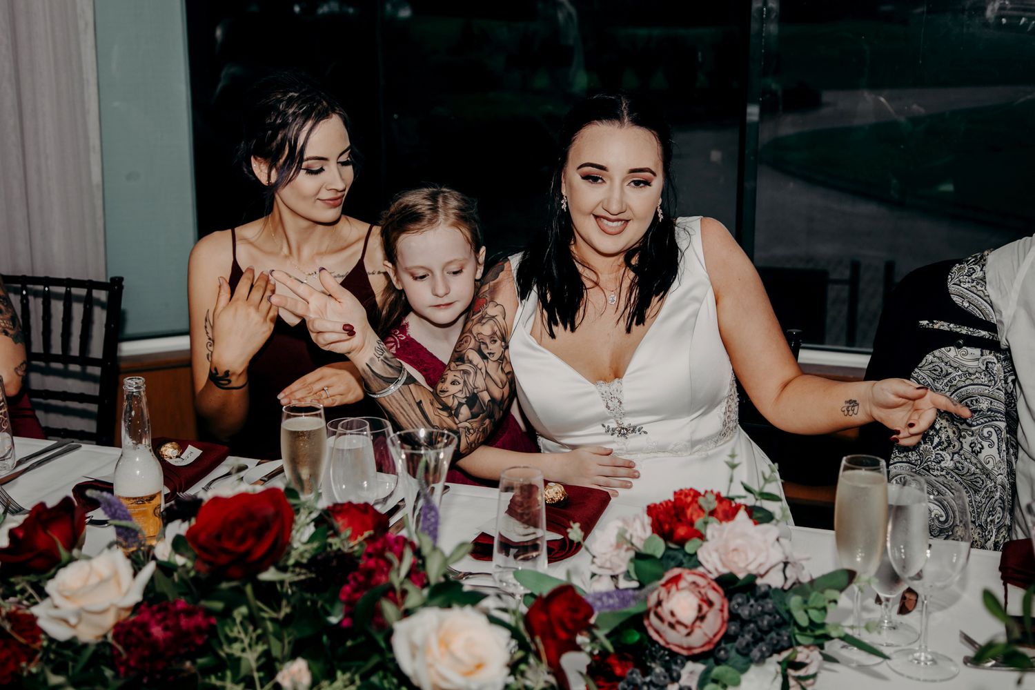 Wedding reception dinner with guests enjoying meal at table decorated with red and white flowers.