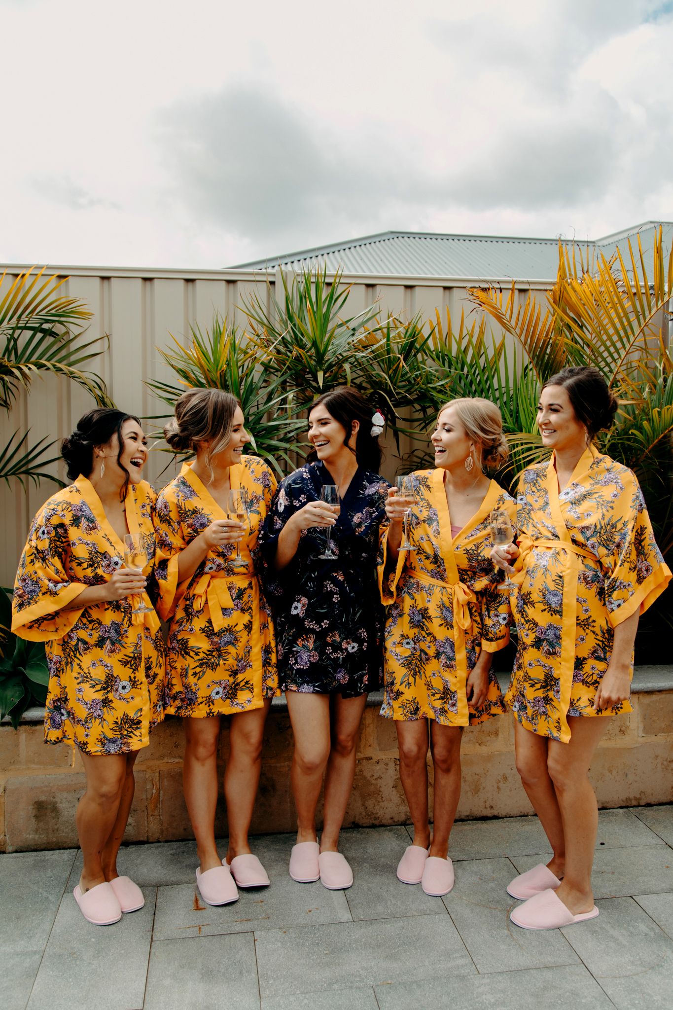 Group wearing yellow floral robes and pink slippers celebrating on outdoor patio.