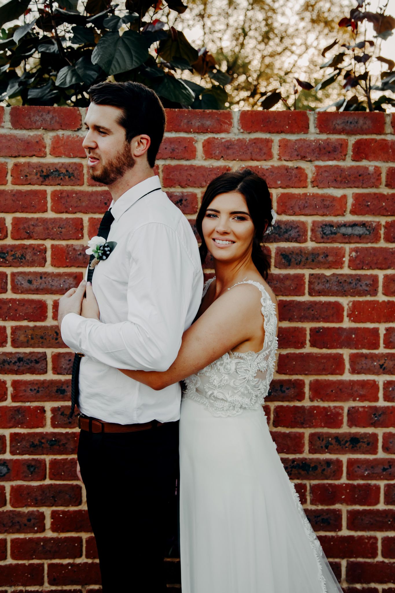 Romantic wedding portrait of couple embracing against rustic brick wall.