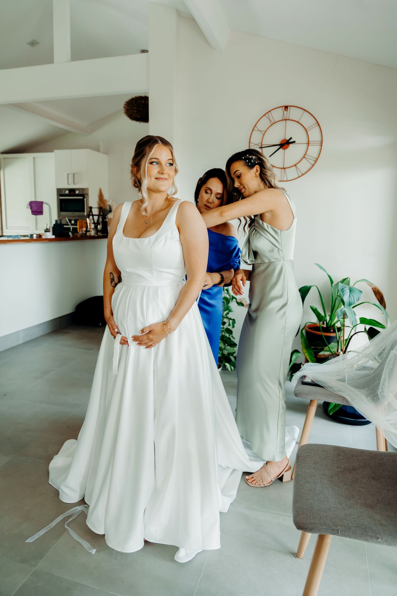 Wedding preparations unfold in a modern white interior with final dress adjustments.