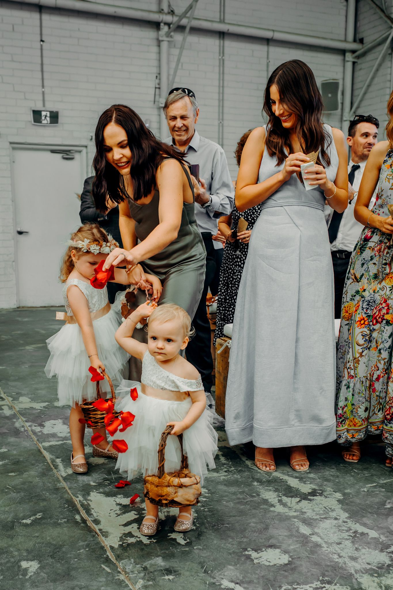 Wedding party helps flower girls scatter red petals in industrial venue.
