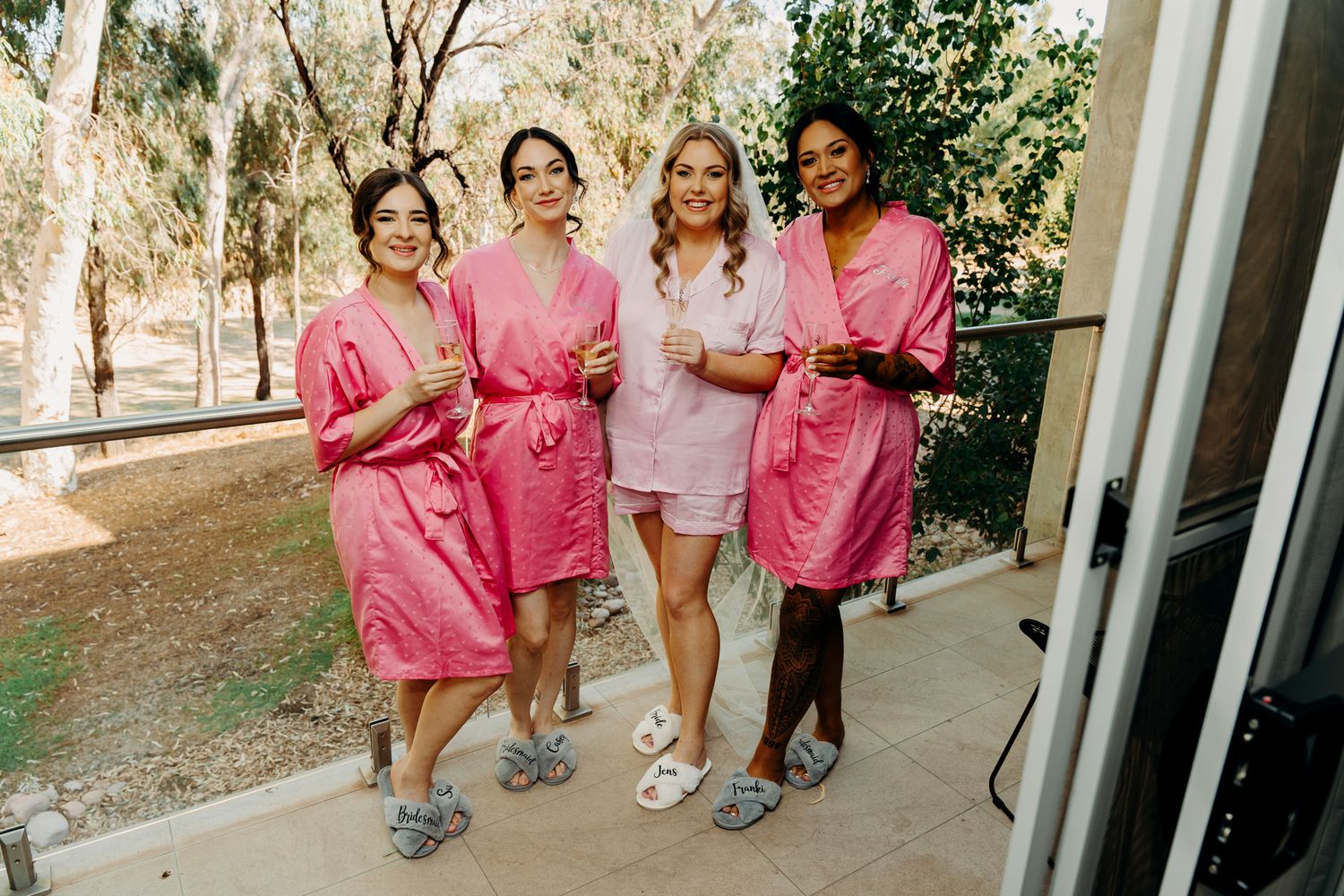 Bridal party in matching pink robes walks together outdoors during pre-wedding preparations.