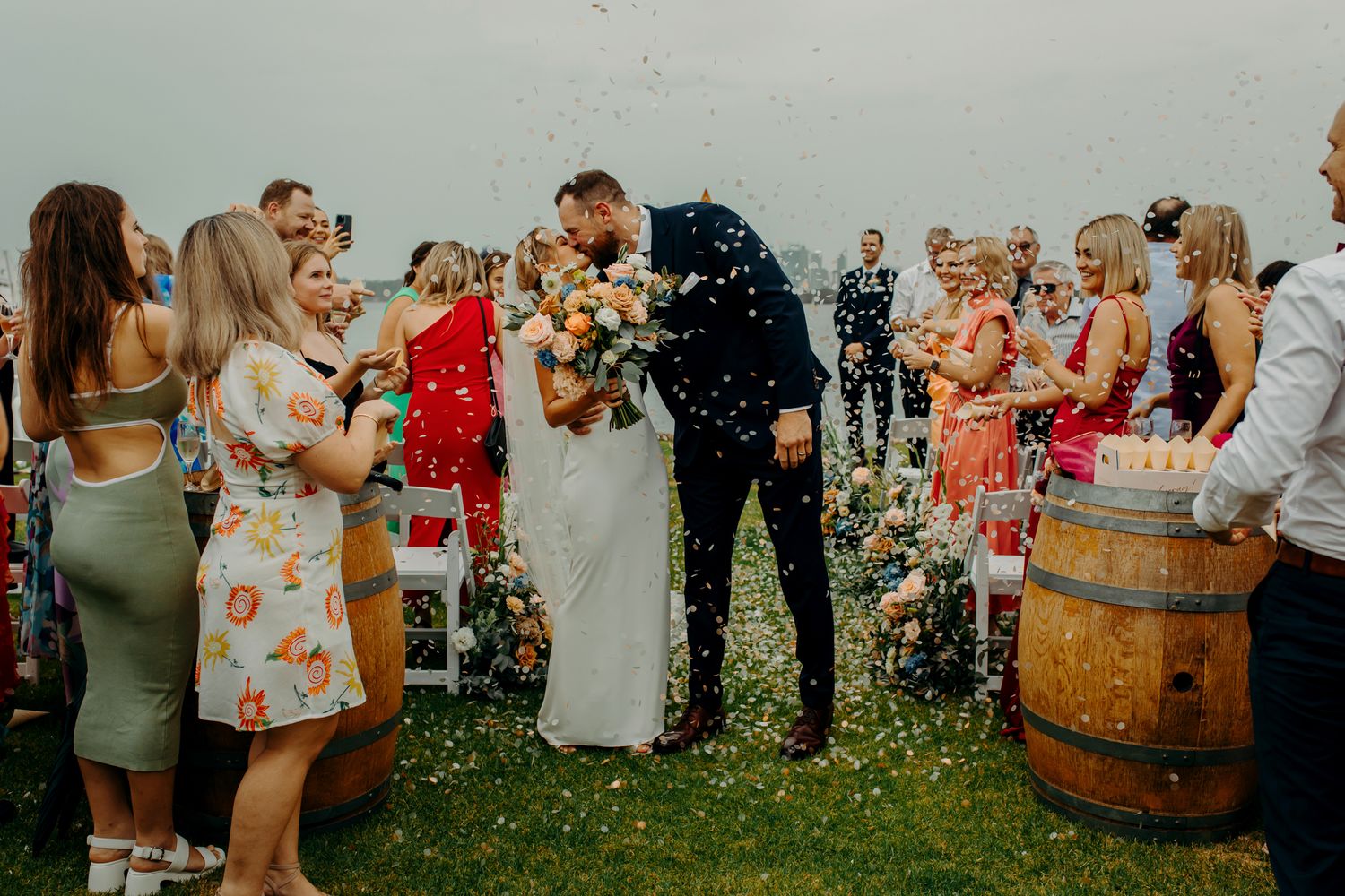 Wedding celebration at yacht club with guests throwing confetti and rustic barrel decor.