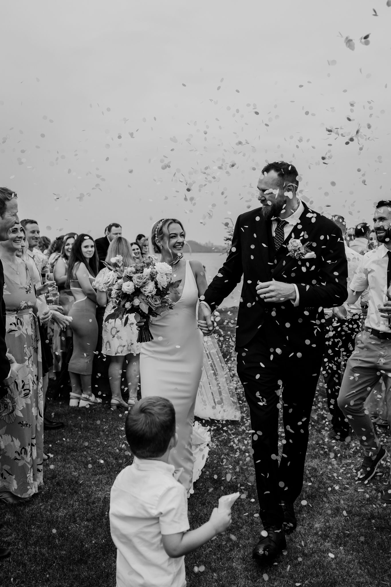 Black and white photo of joyful wedding celebration with confetti and guests.
