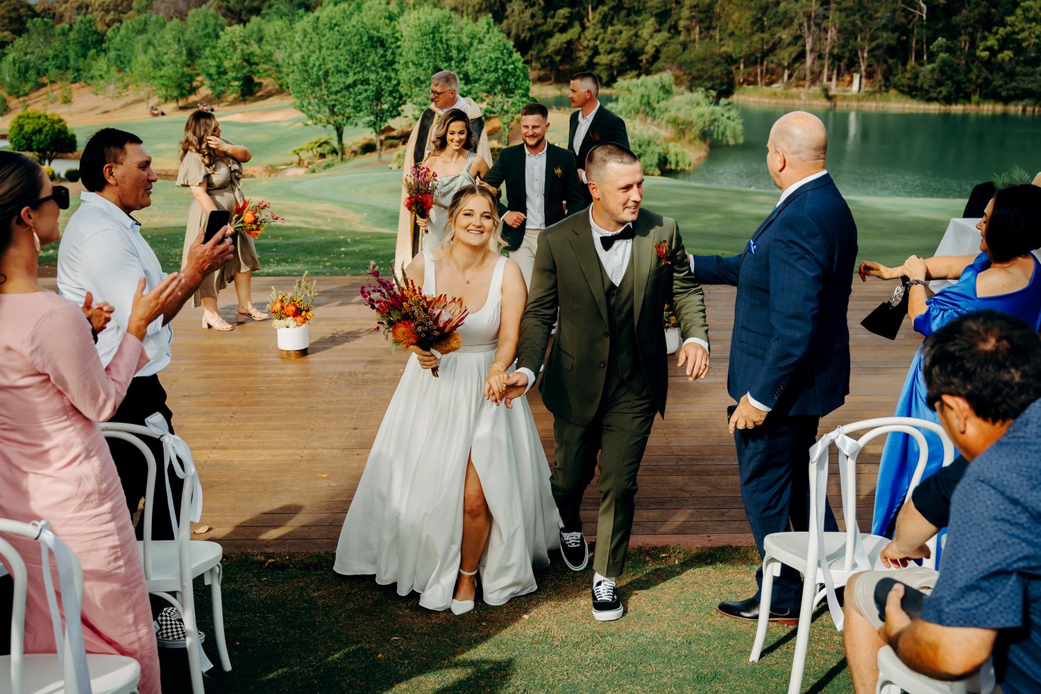 Wedding guests celebrate as newlyweds walk down the aisle on an outdoor deck.