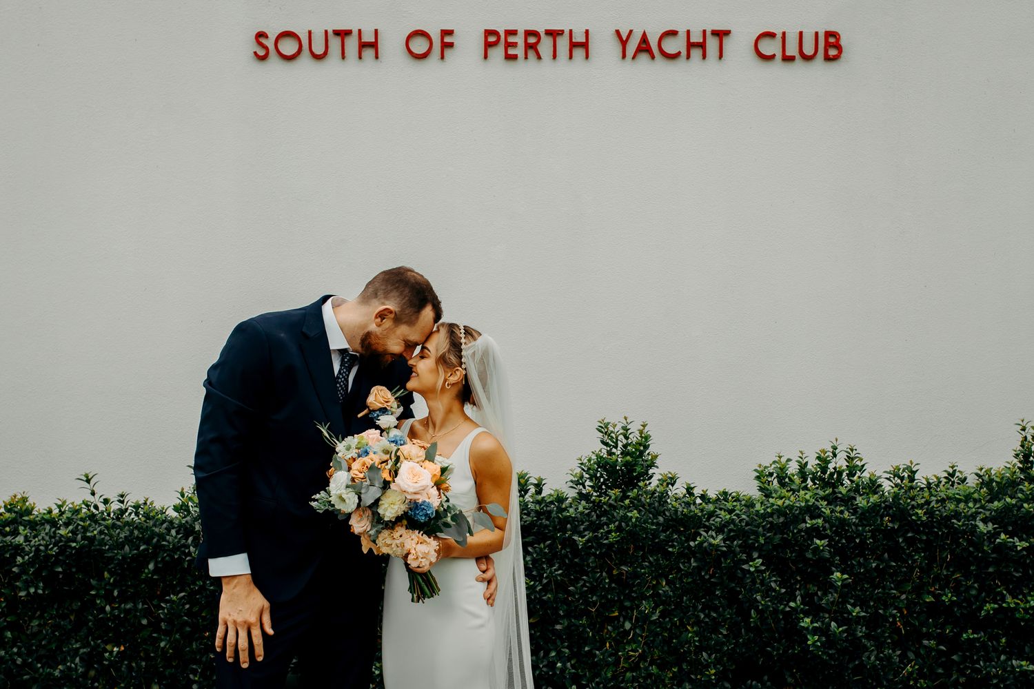 Romantic moment captured outside South of Perth Yacht Club with elegant floral bouquet.