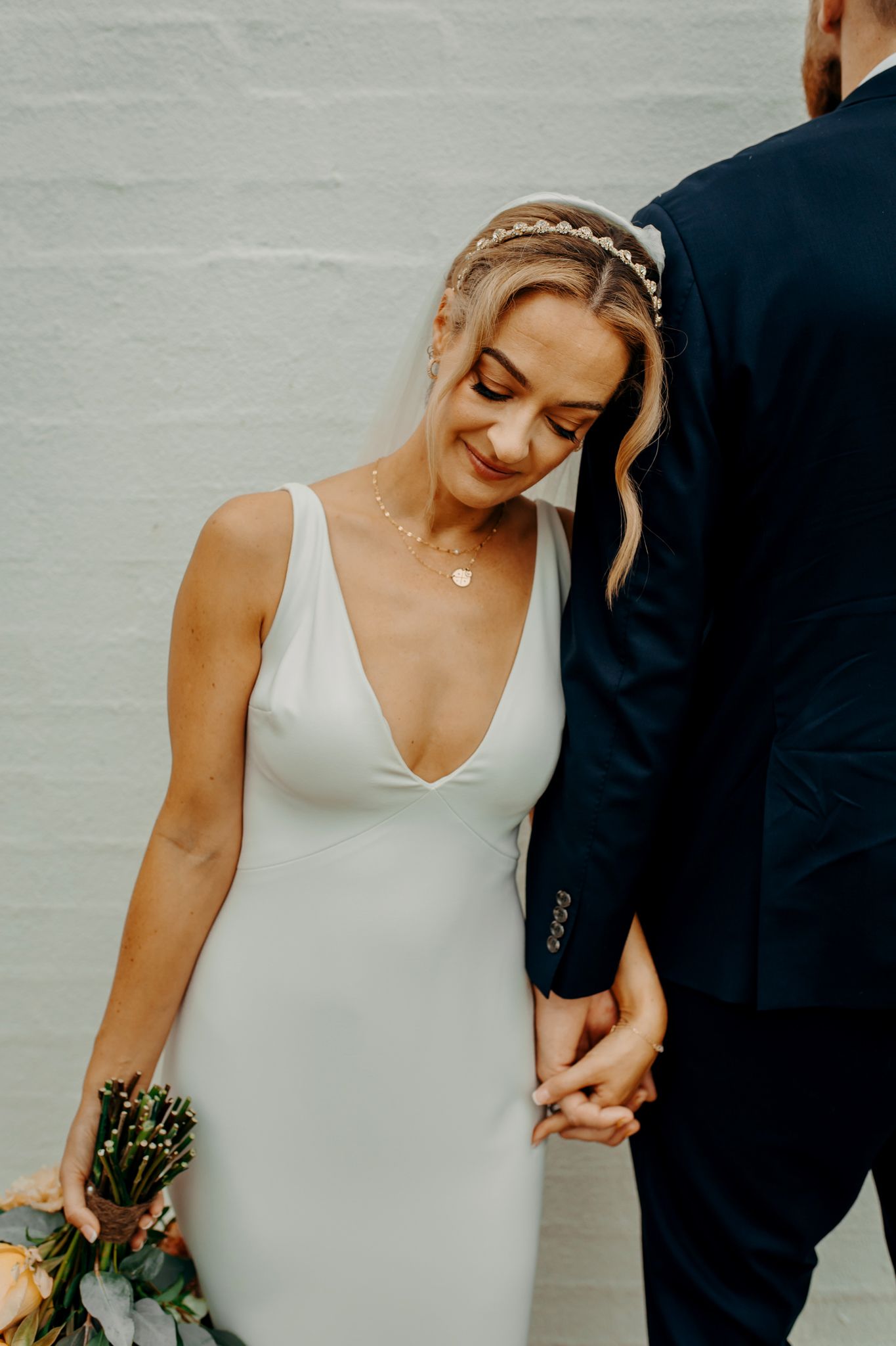 Elegant bride in sleek white dress with intricate braided hairstyle holds bouquet.