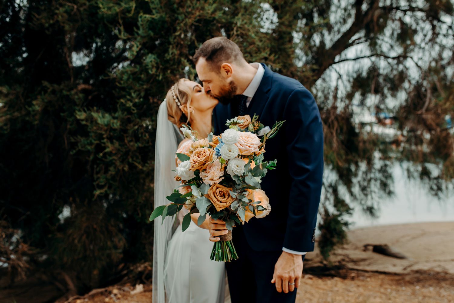 Wedding couple embraces during golden hour holding peach and cream floral bouquet.