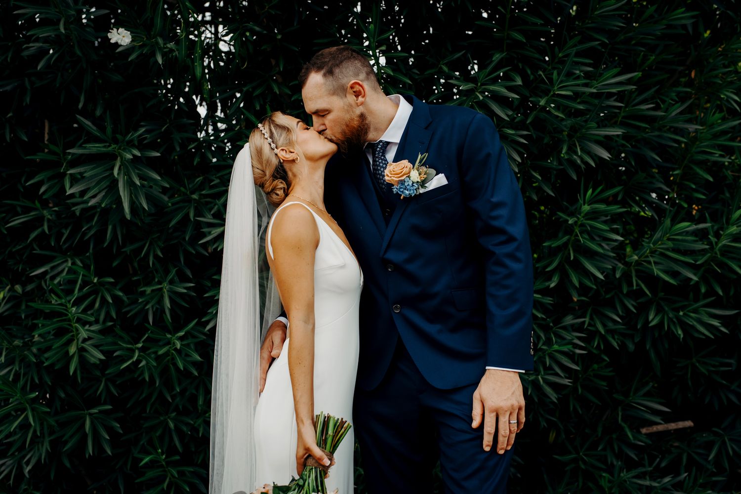 Intimate wedding portrait with tropical greenery backdrop and elegant white dress.