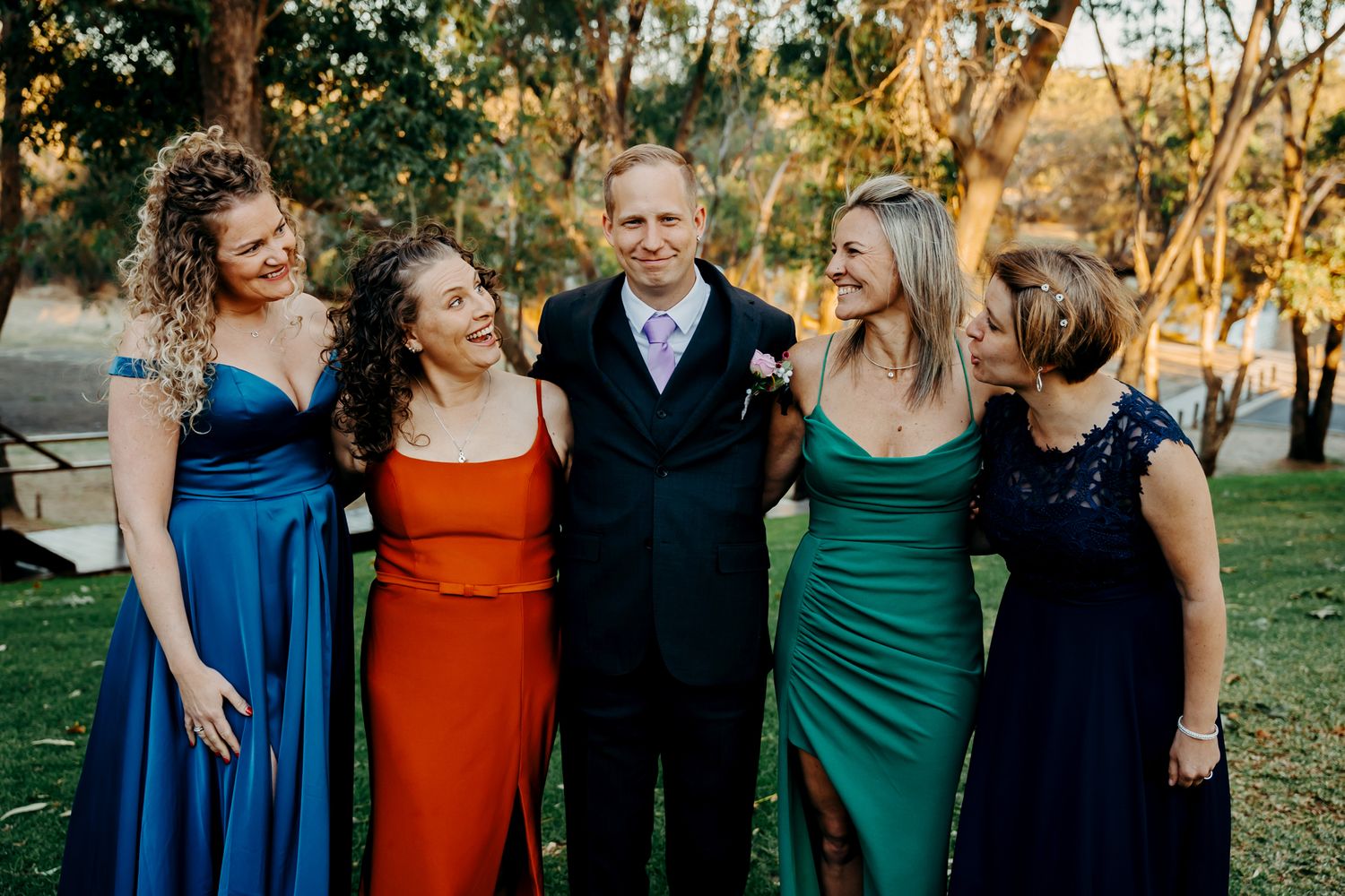 Wedding party in coordinating formal attire poses together outdoors at sunset.