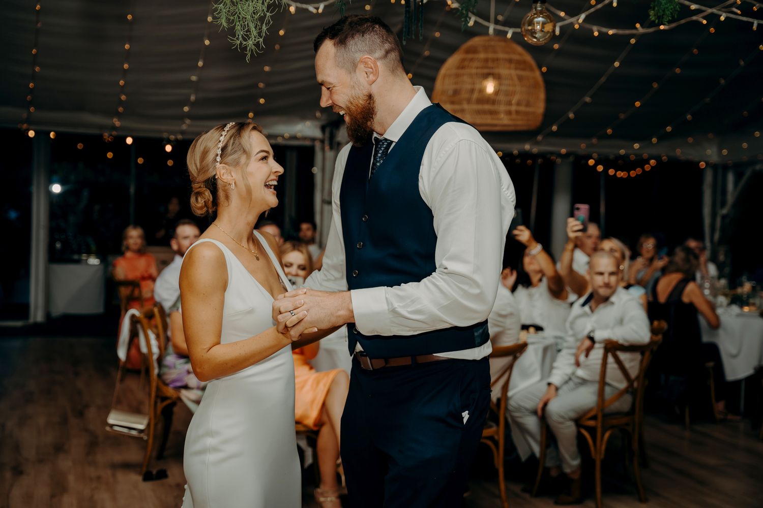 A couple shares an intimate dance moment at their wedding reception under string lights.