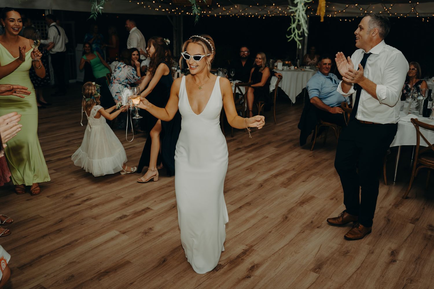 A bride in a sleek white dress dances energetically at her wedding reception.