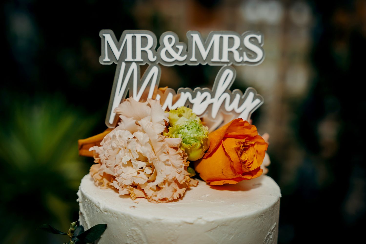 Wedding cake topper reading Mr & Mrs Murphy with orange rose decoration.