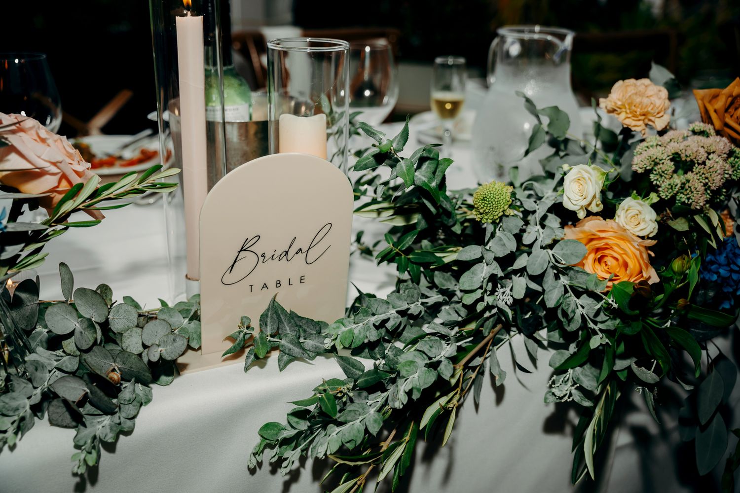 Elegant wedding table setting with eucalyptus garland and peach roses.