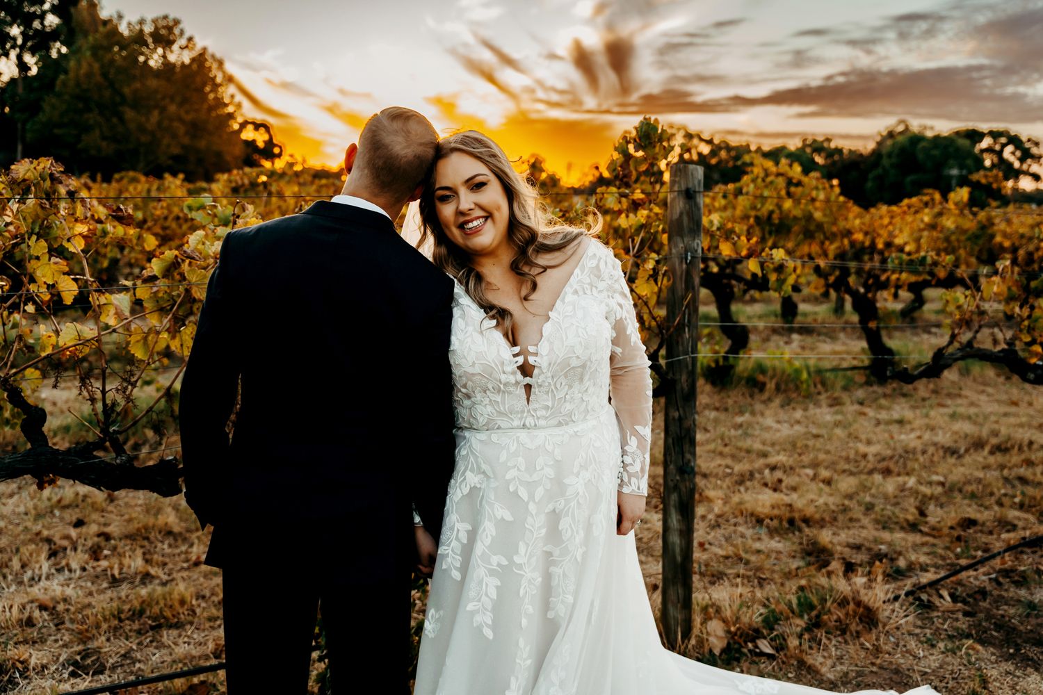 Intimate wedding portrait of couple embracing among vineyard rows at sunset.