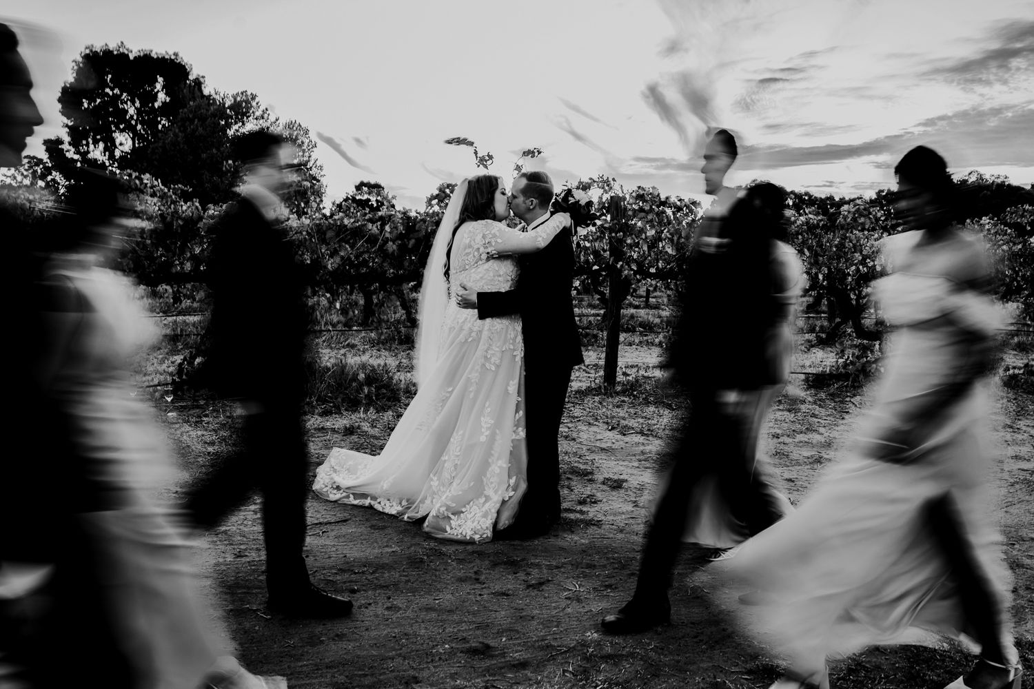 Artistic black and white photo of wedding party in motion around central couple.