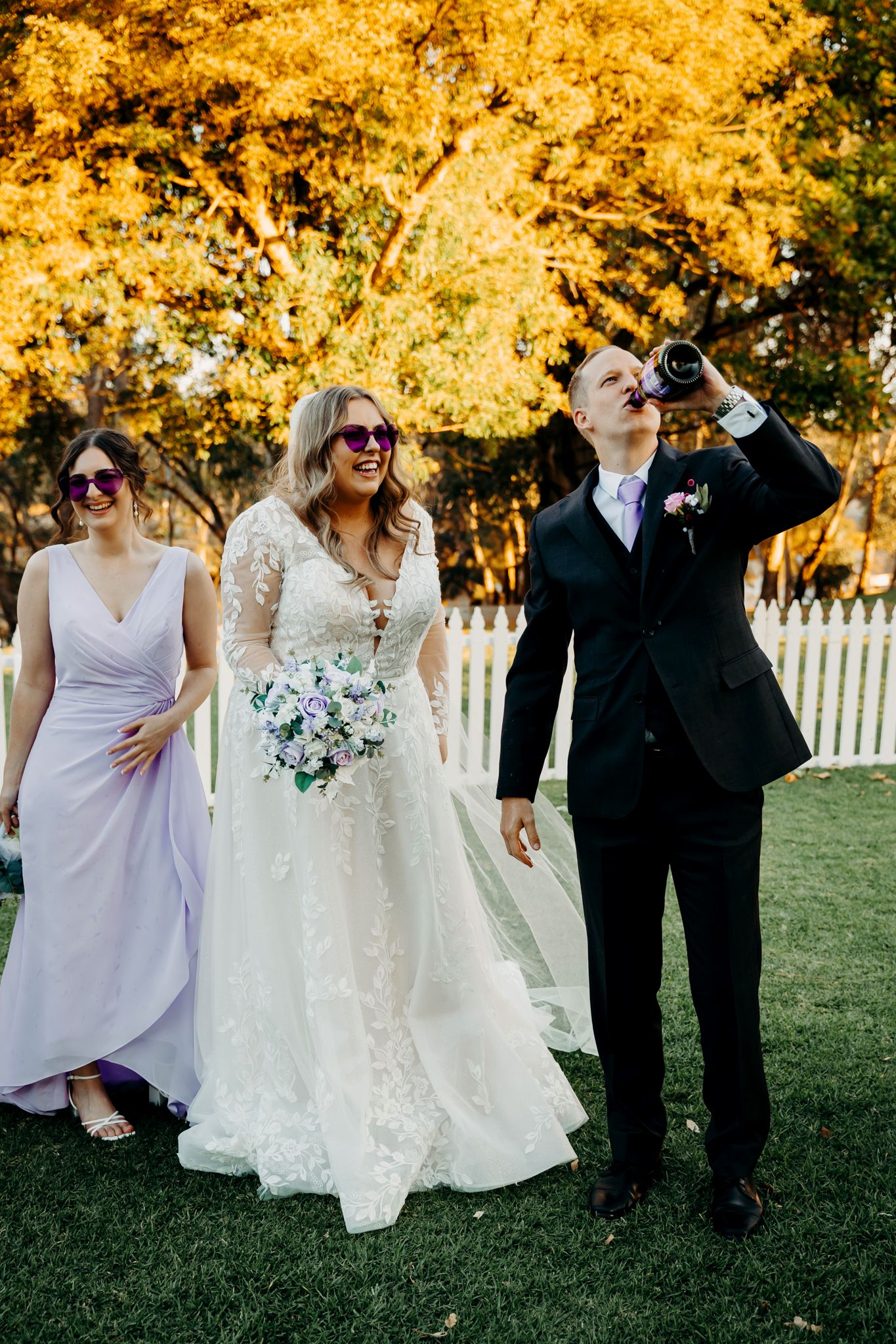 Wedding party poses playfully in front of autumn trees with golden foliage.