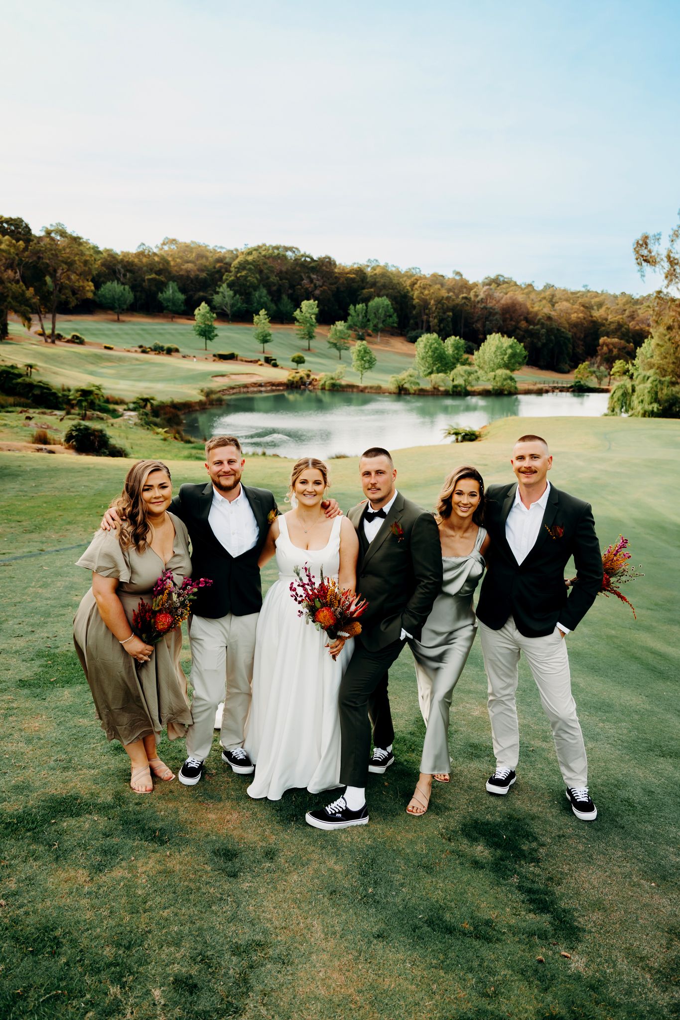 Wedding party poses together on a scenic golf course with rolling hills and a pond in the background.