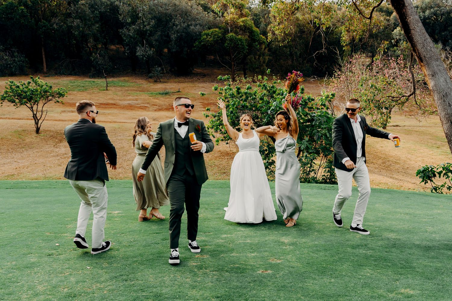 Wedding party walks across a green lawn in casual celebratory style.