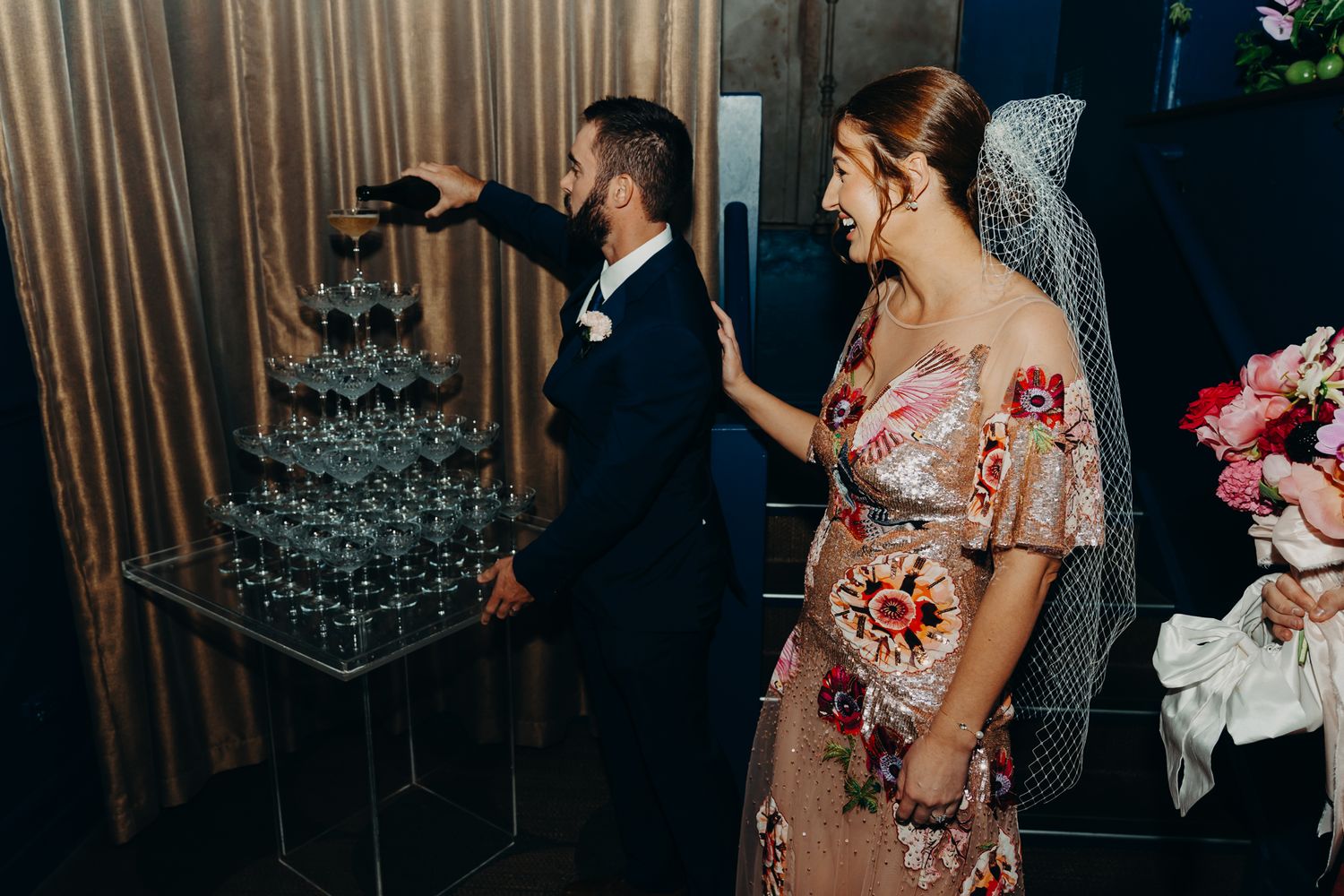 A couple admires a champagne tower display at their wedding reception.