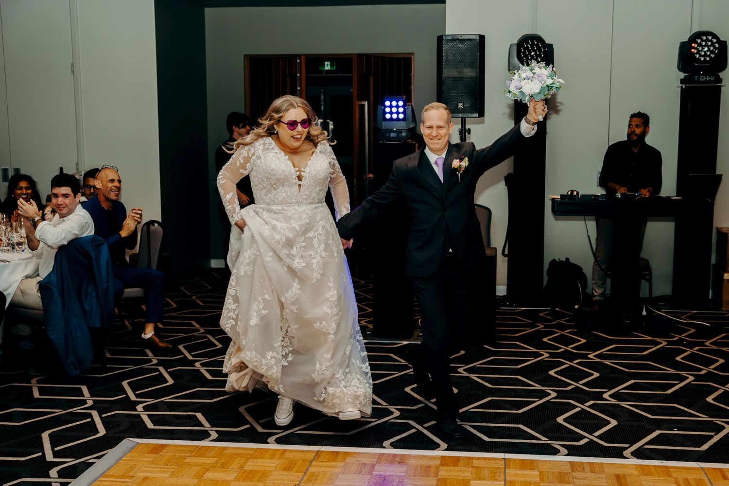 A newlywed couple makes their grand entrance at their wedding reception on a geometric patterned dance floor.