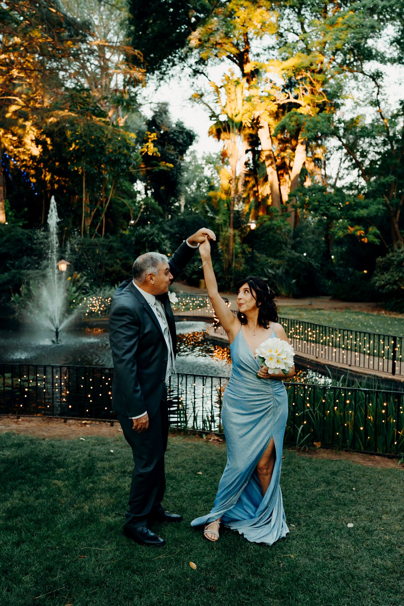 Couple dancing playfully on a grassy lawn at sunset with Spanish moss draped trees in the background.