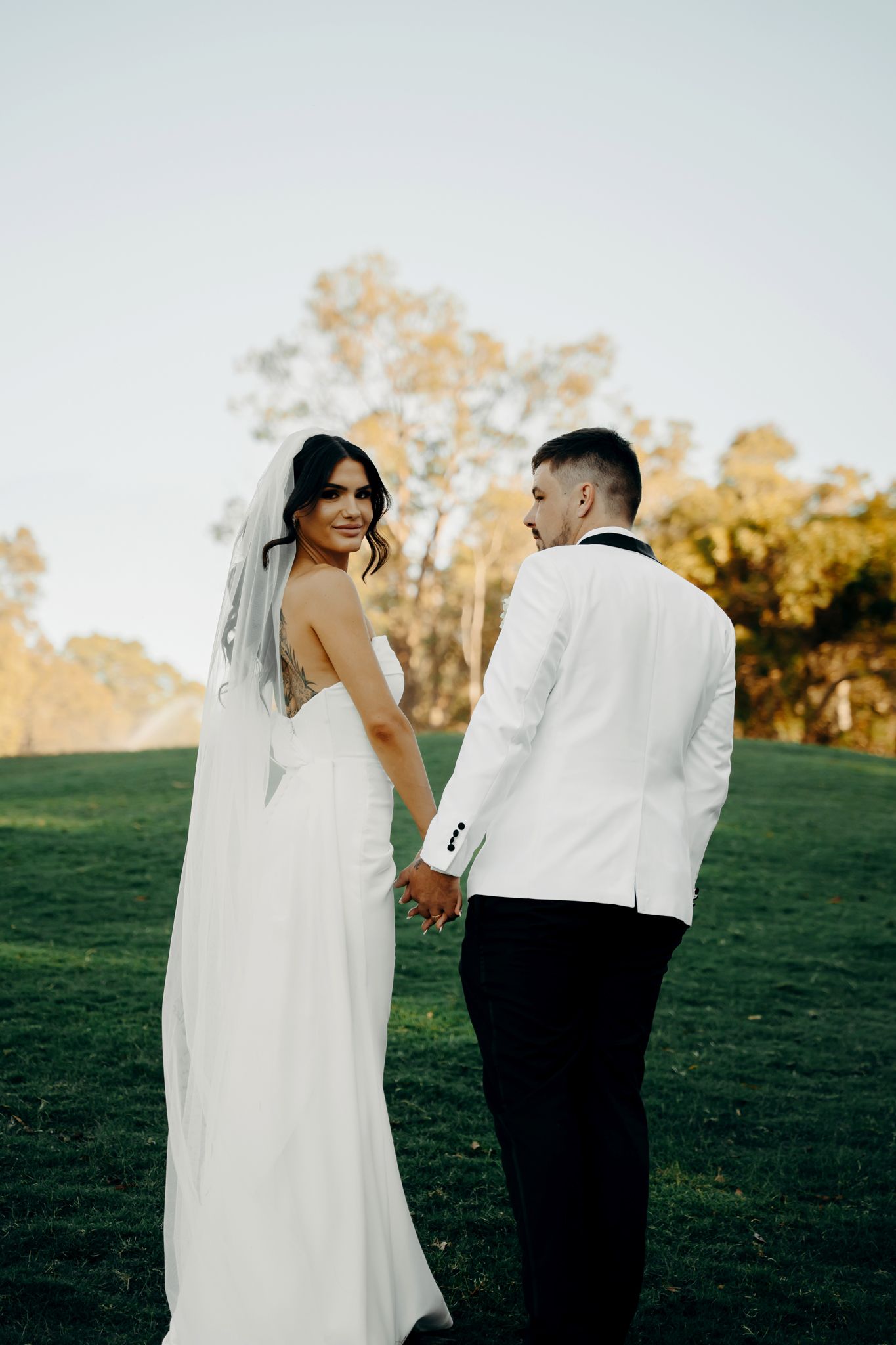 Newlyweds share candid moments on a grassy hillside during golden hour photography session.