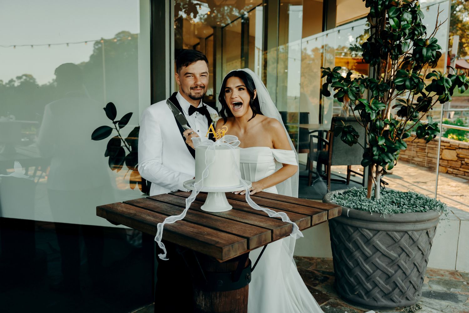 A wedding couple poses together in an elegant indoor venue decorated with greenery and natural light.