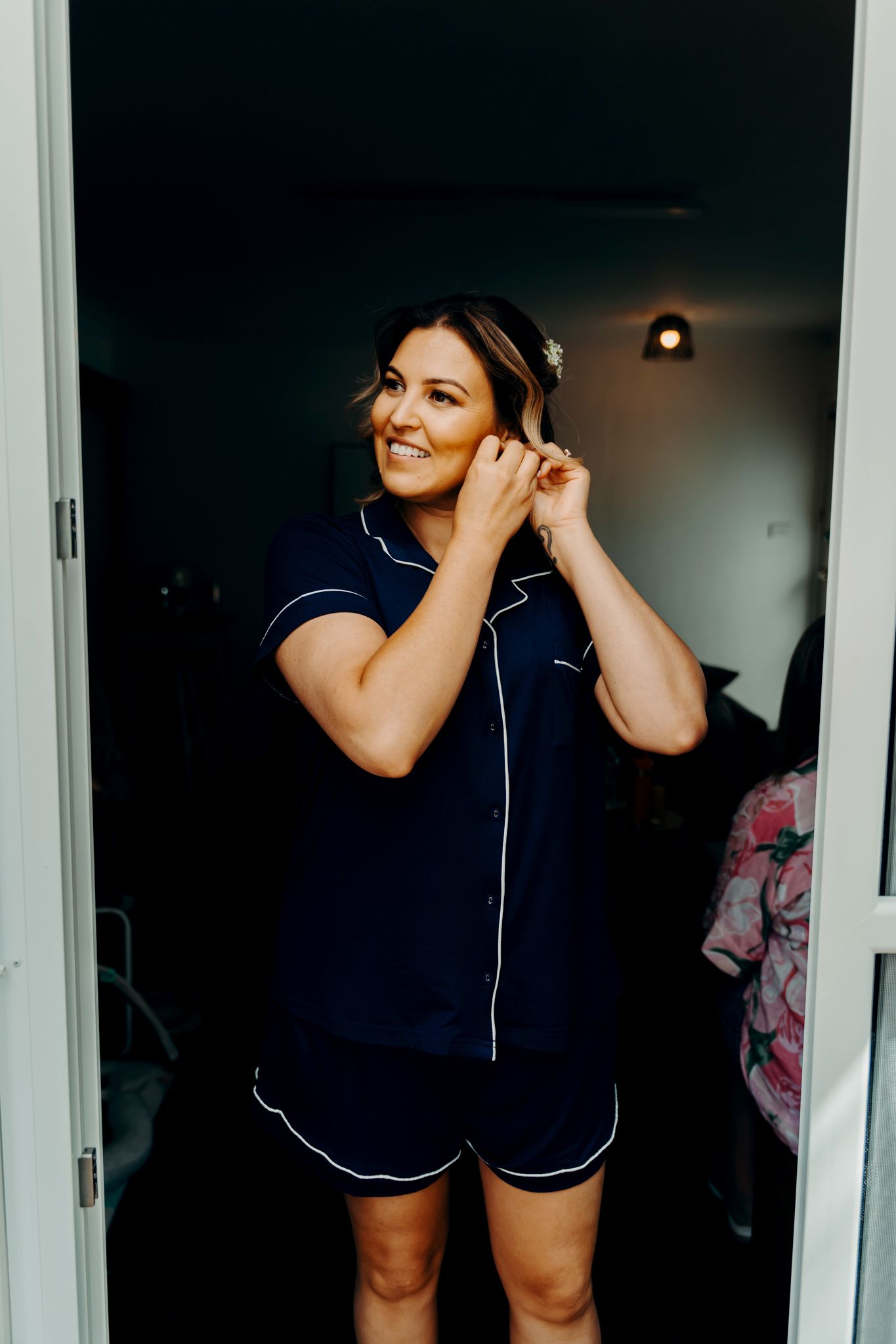 Someone in navy blue pajamas getting ready in front of a mirror in a dimly lit room.