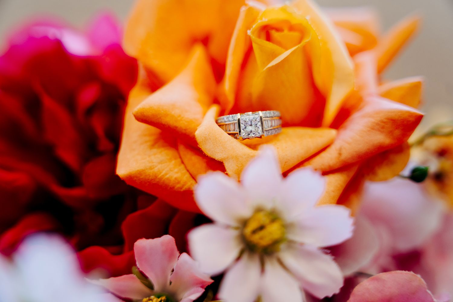 Vibrant orange roses and delicate pink blossoms create a romantic floral arrangement with a sparkling diamond ring.
