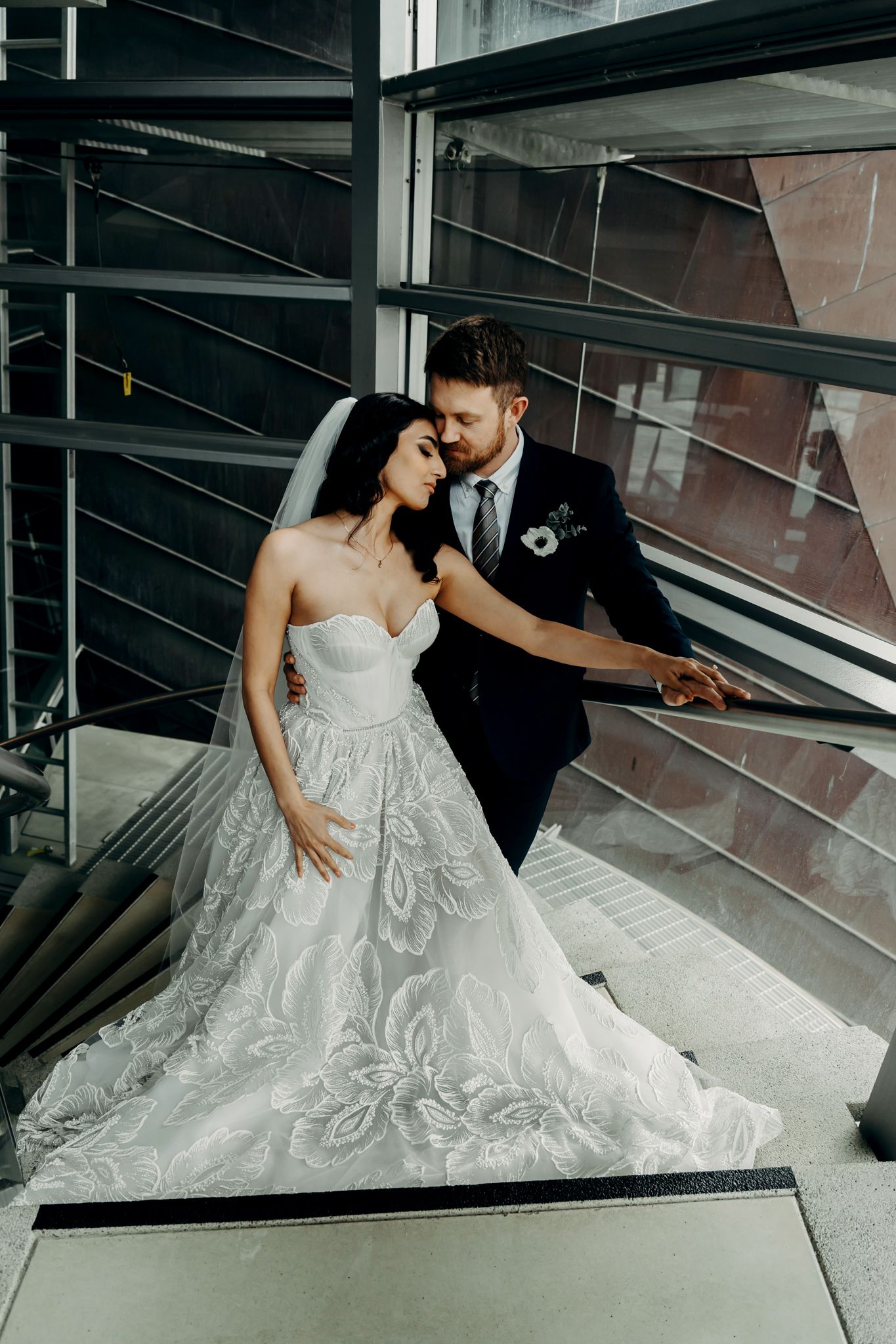 Intimate wedding portrait on modern staircase with dramatic lighting and architectural elements.