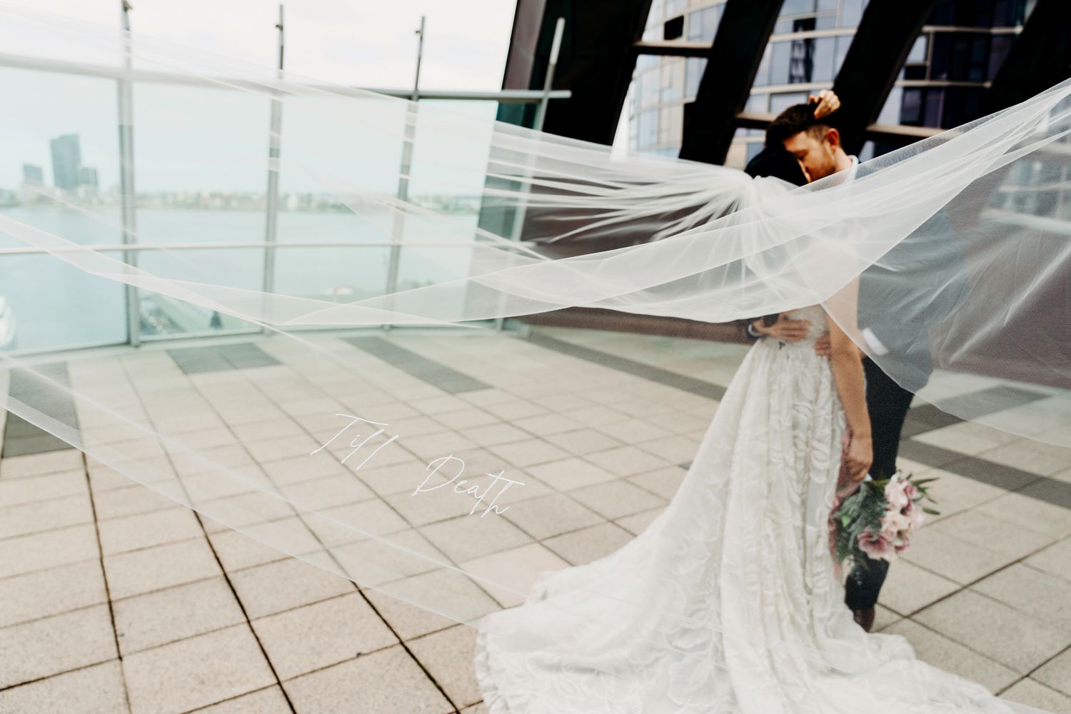 Flowing wedding veil catches wind on modern rooftop terrace with cityscape view.