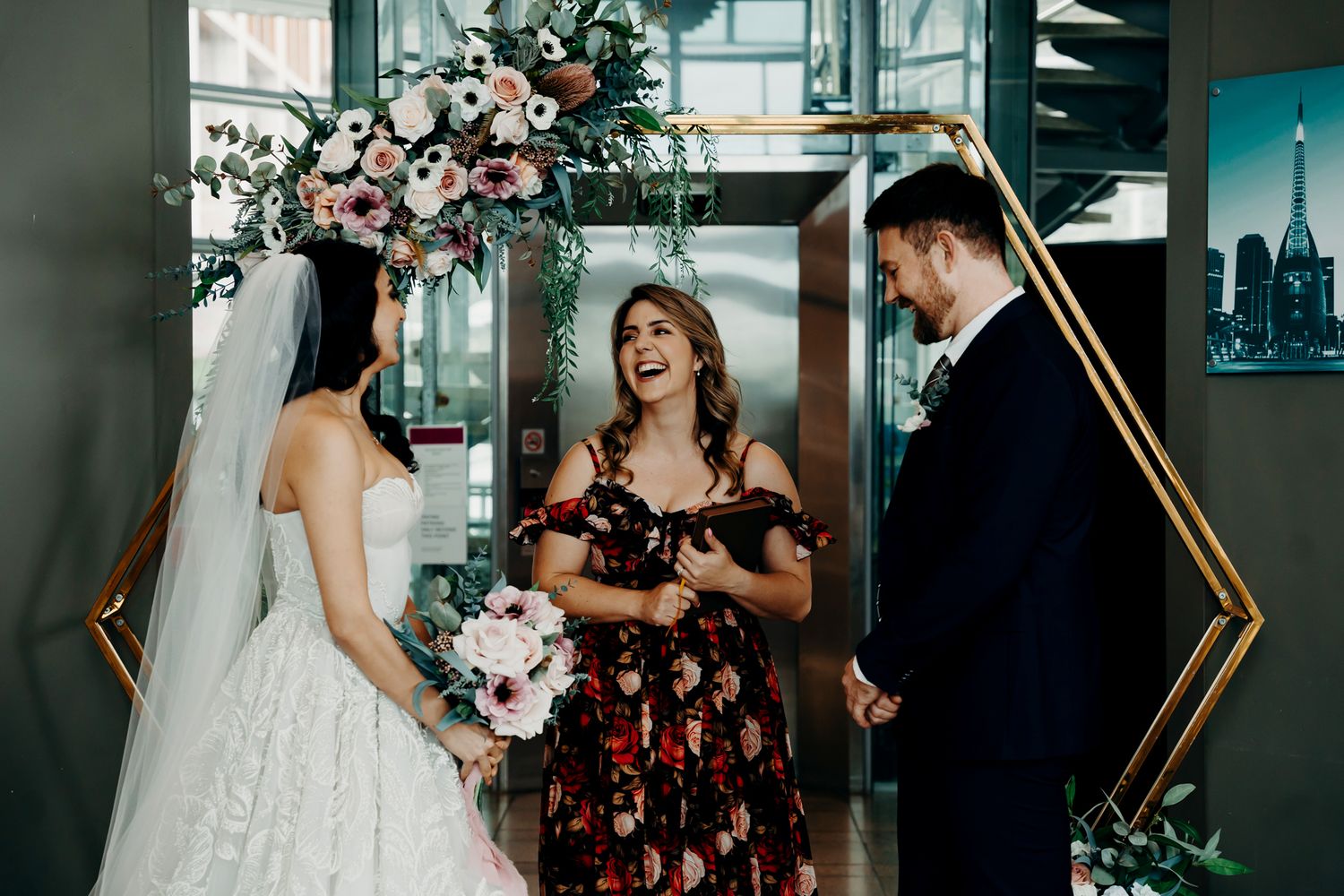 Wedding ceremony in modern indoor setting with geometric gold frame and floral arrangements.