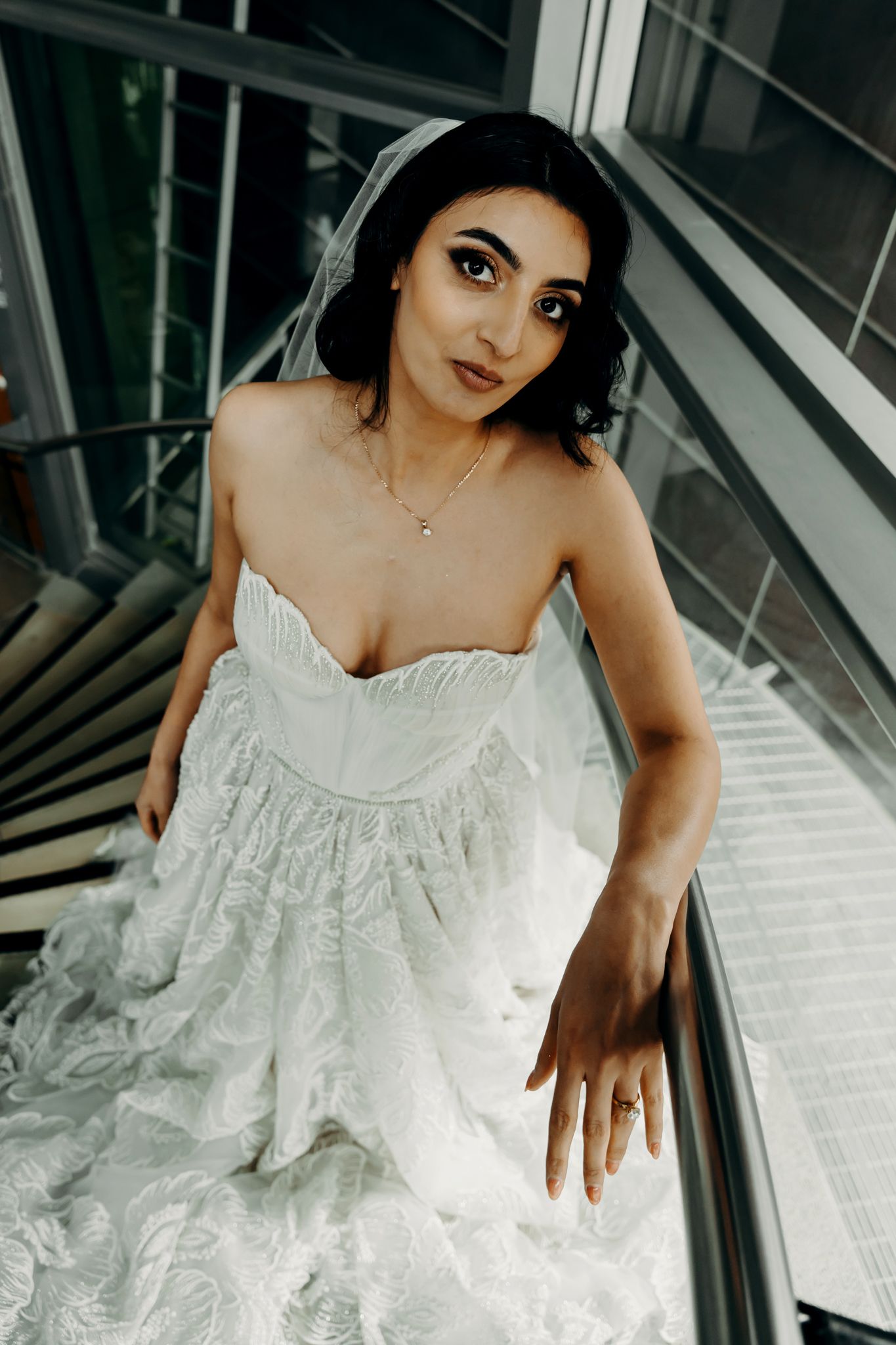 Bridal portrait on staircase showcasing intricate lace wedding gown details.