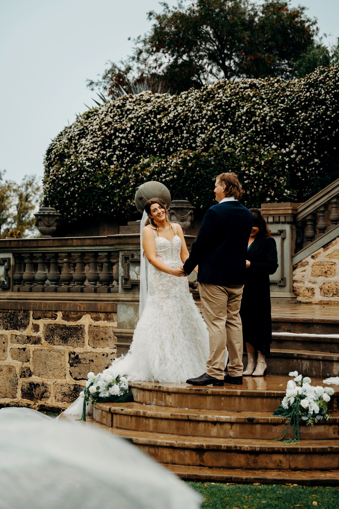Wedding couple posing for photos on stone steps with greenery and floral decorations.