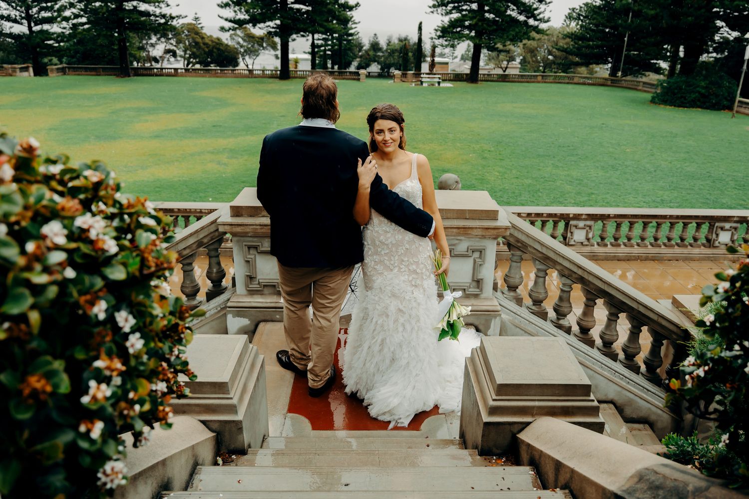 Couple sharing an intimate moment on a stone balcony overlooking a lush green garden setting.