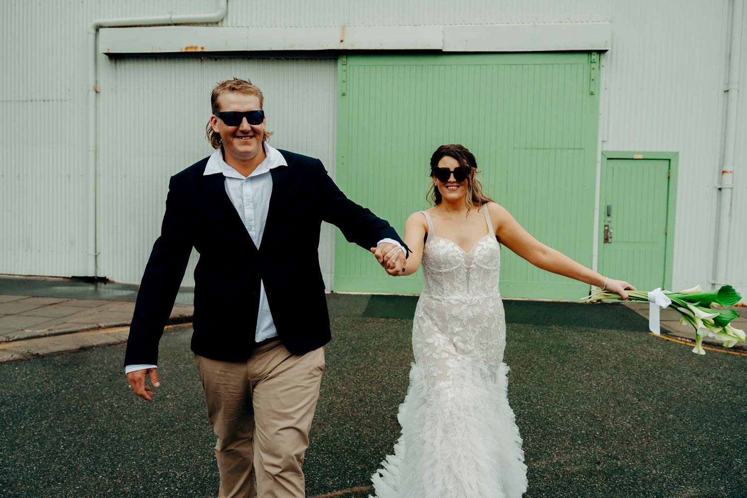 Wedding couple playfully dances and twirls on a dark asphalt surface.