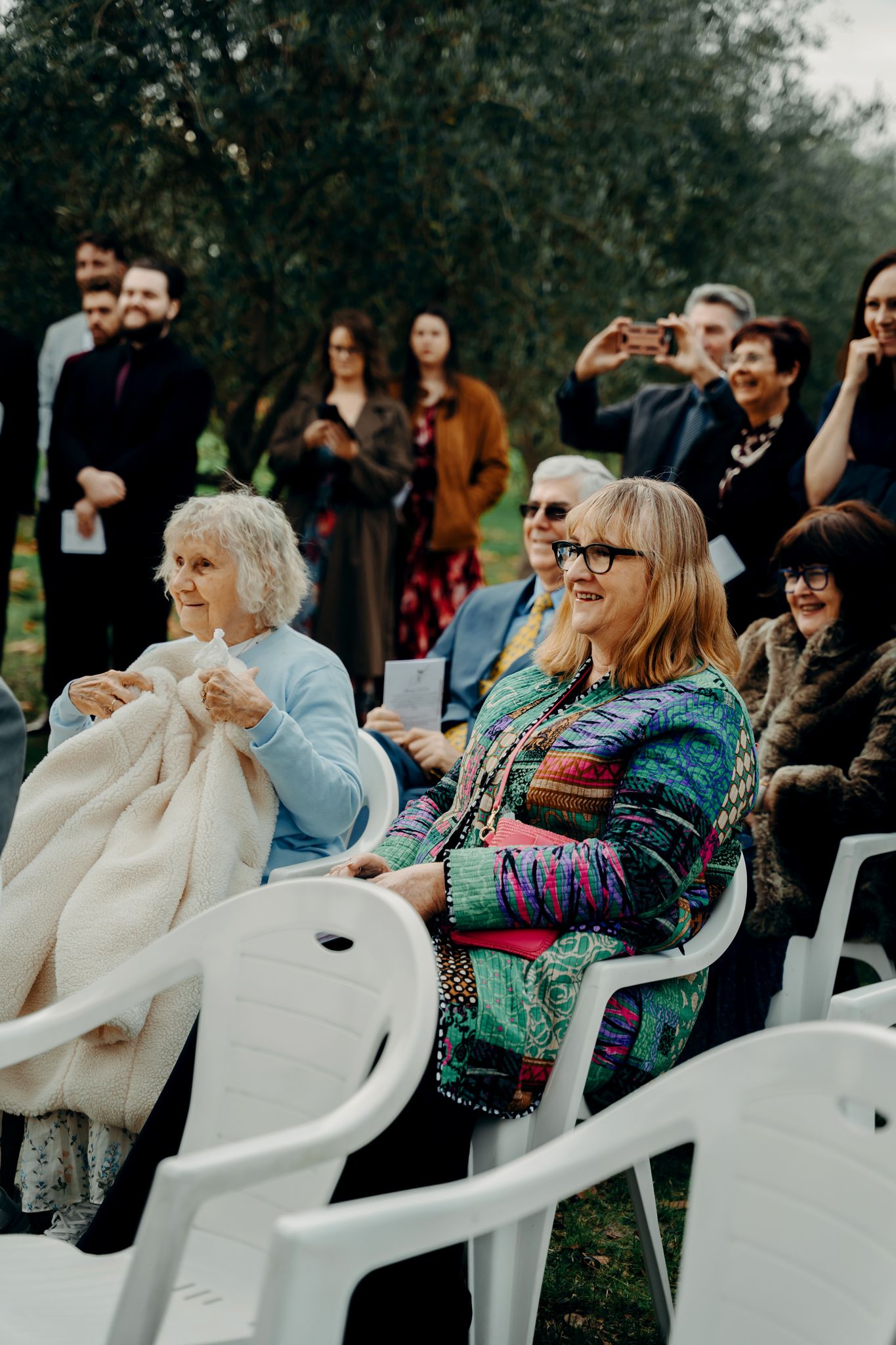 People sitting in white plastic chairs outdoors enjoying what appears to be a celebratory gathering or event.