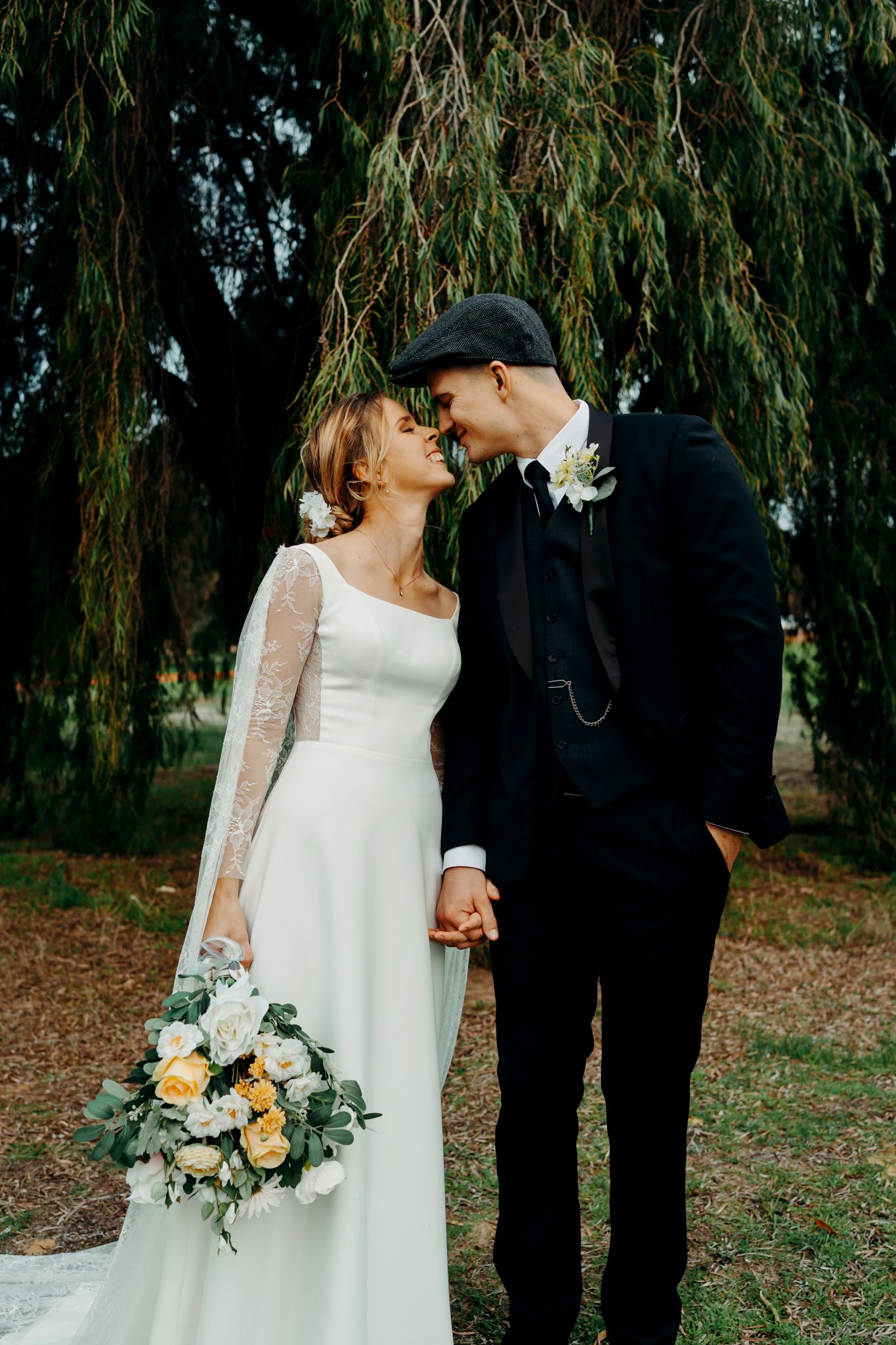 Romantic wedding couple sharing intimate moments under a willow tree in an outdoor garden setting.
