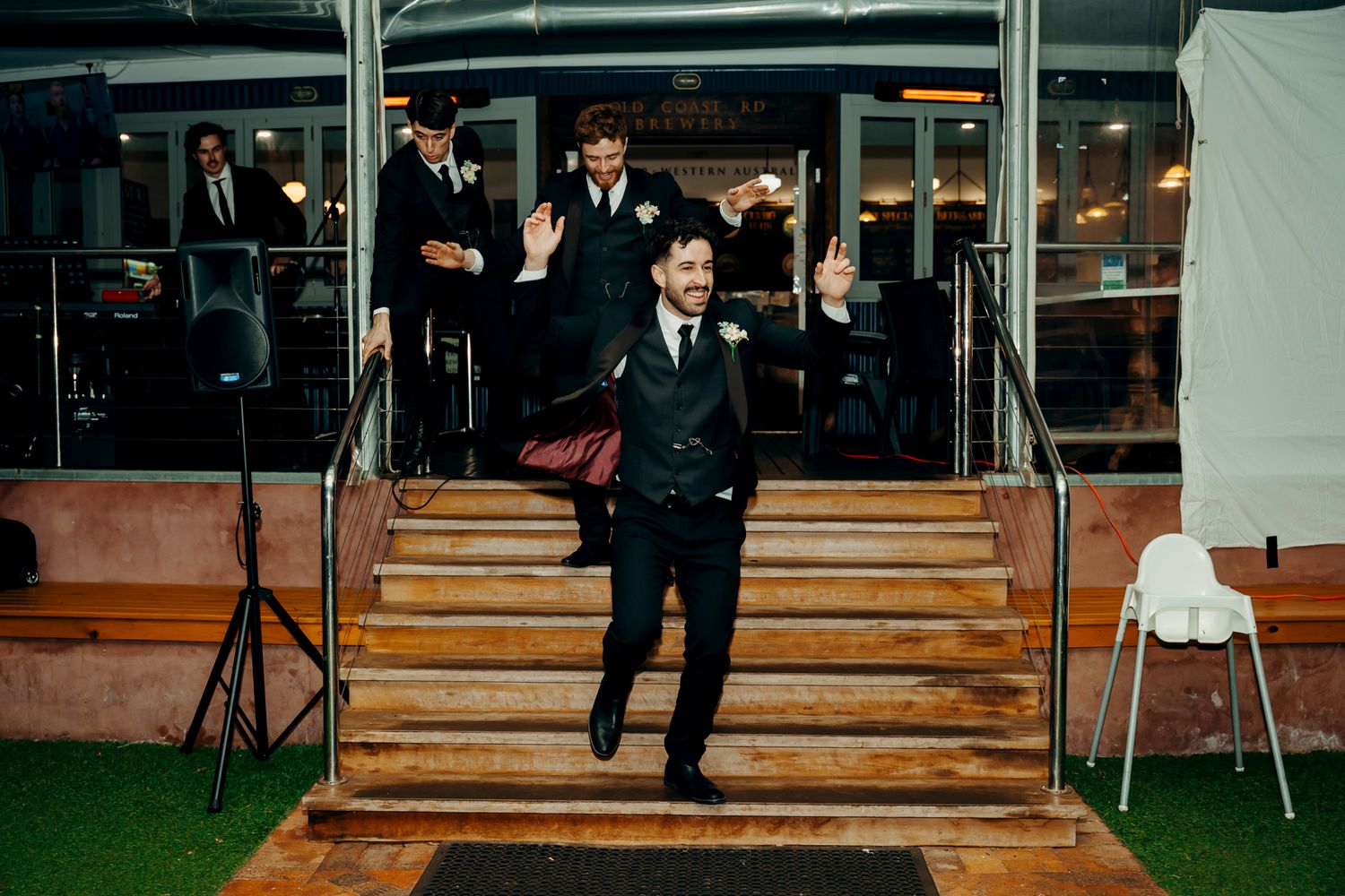 Sequence of still photographs showing a wedding entrance down wooden stairs at twilight with strings of lights.