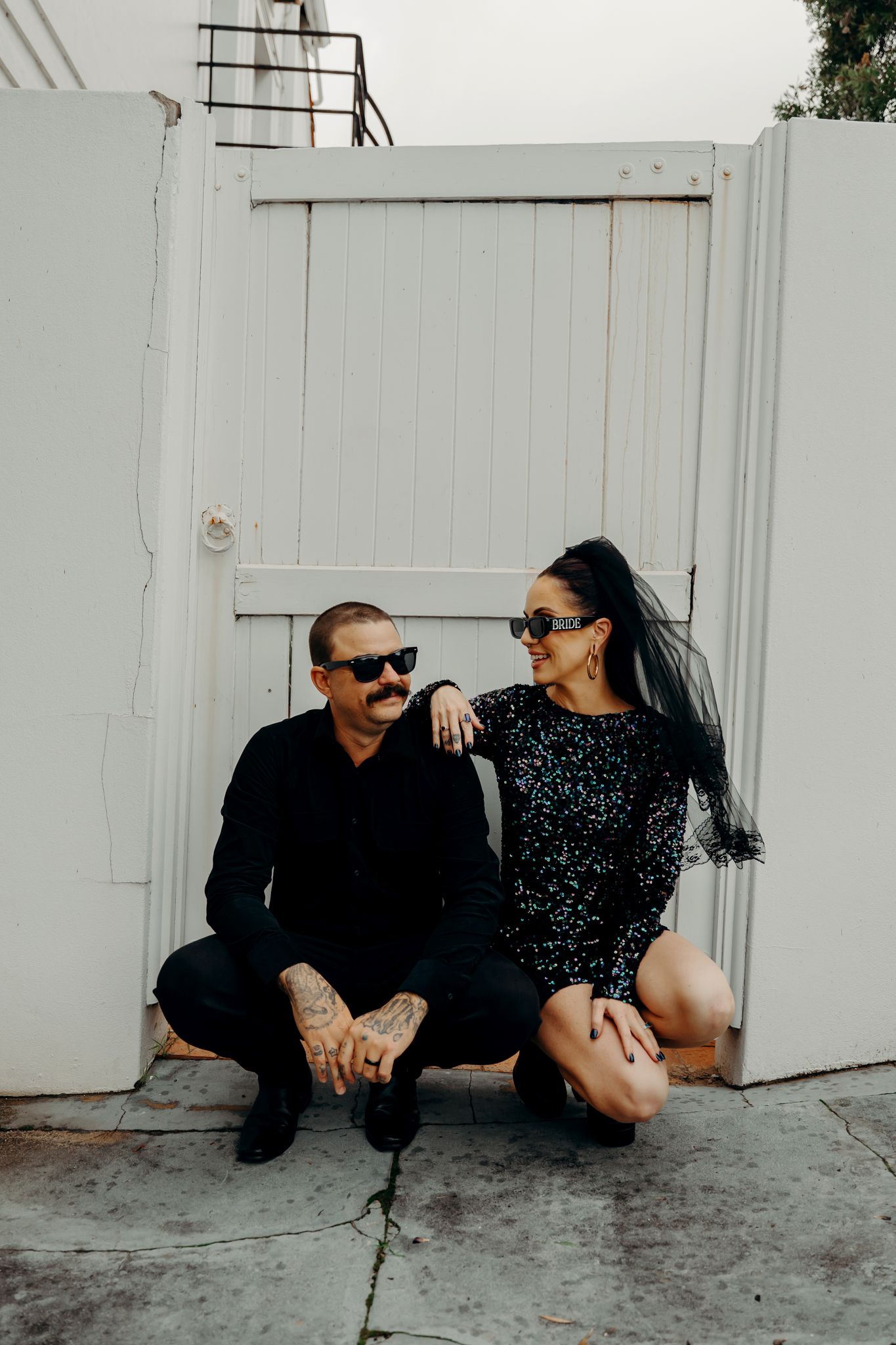 A stylish couple in sunglasses embrace in a romantic series of black and white photos against a white wall.