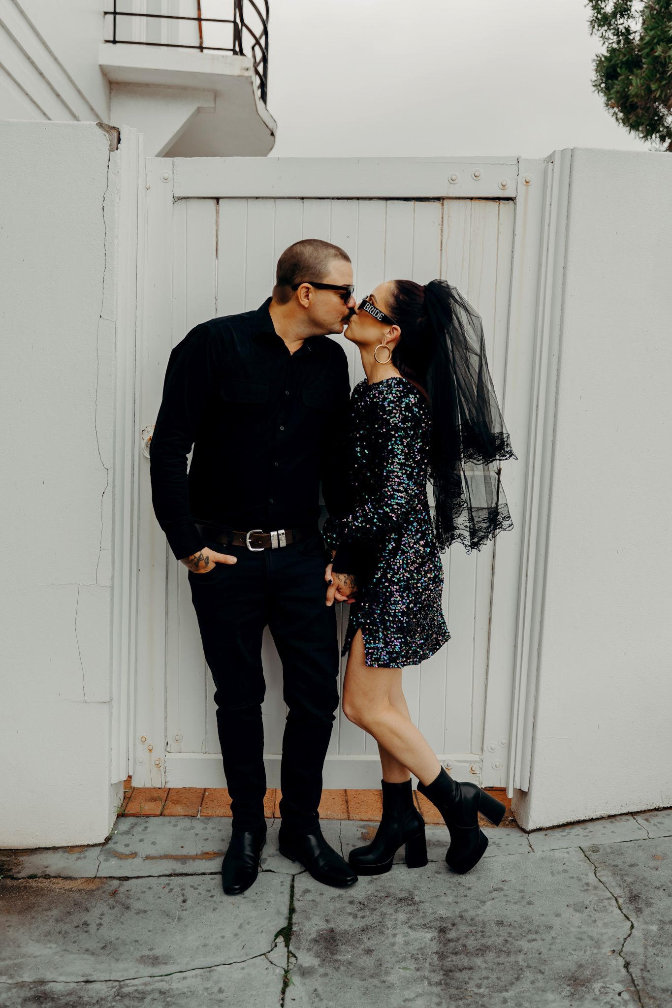 A couple in black attire share intimate moments in a progression of photographs by a white wall.