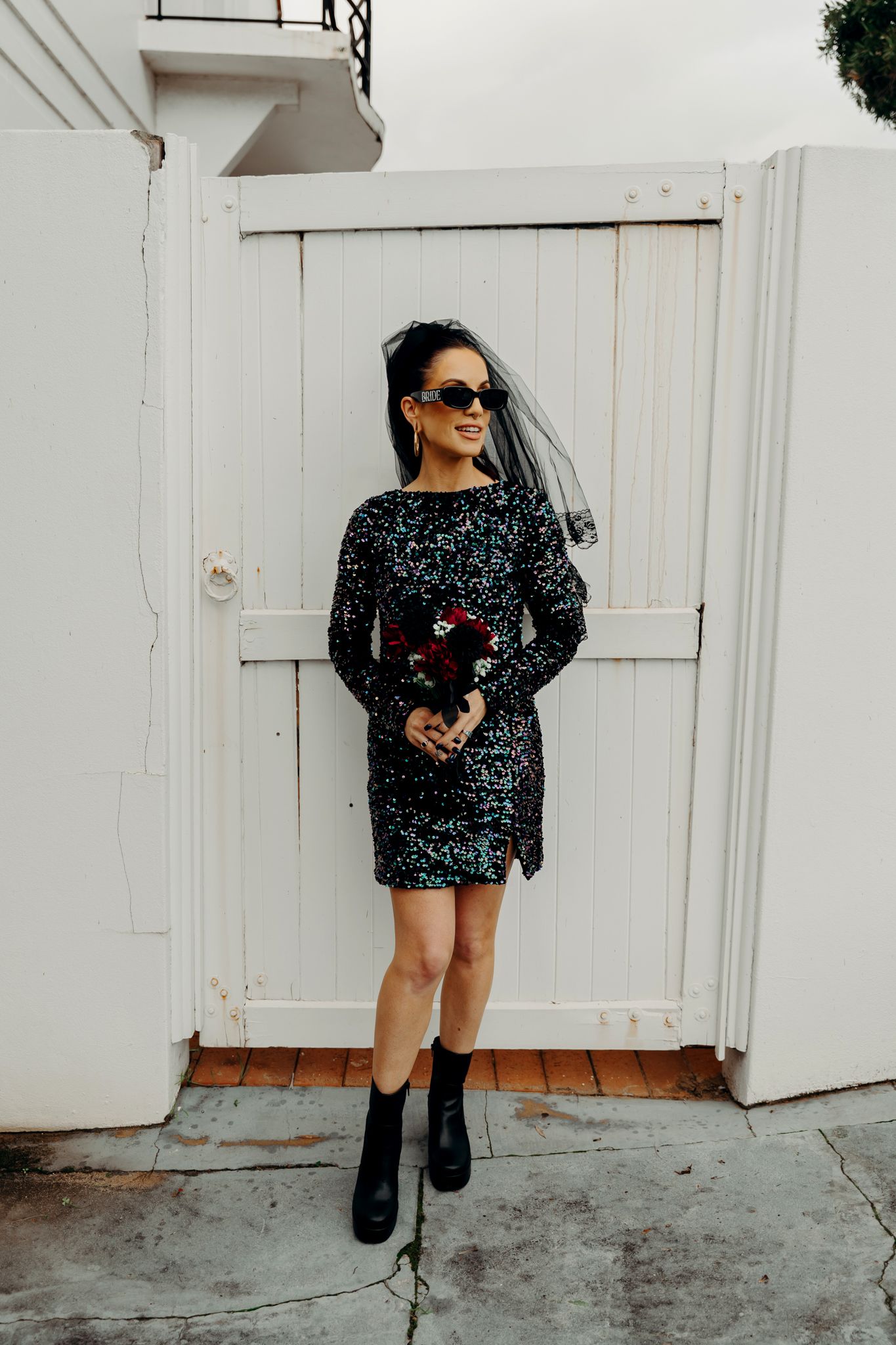 A person in a sparkly black sequined mini dress and boots poses against a white wall in multiple shots.