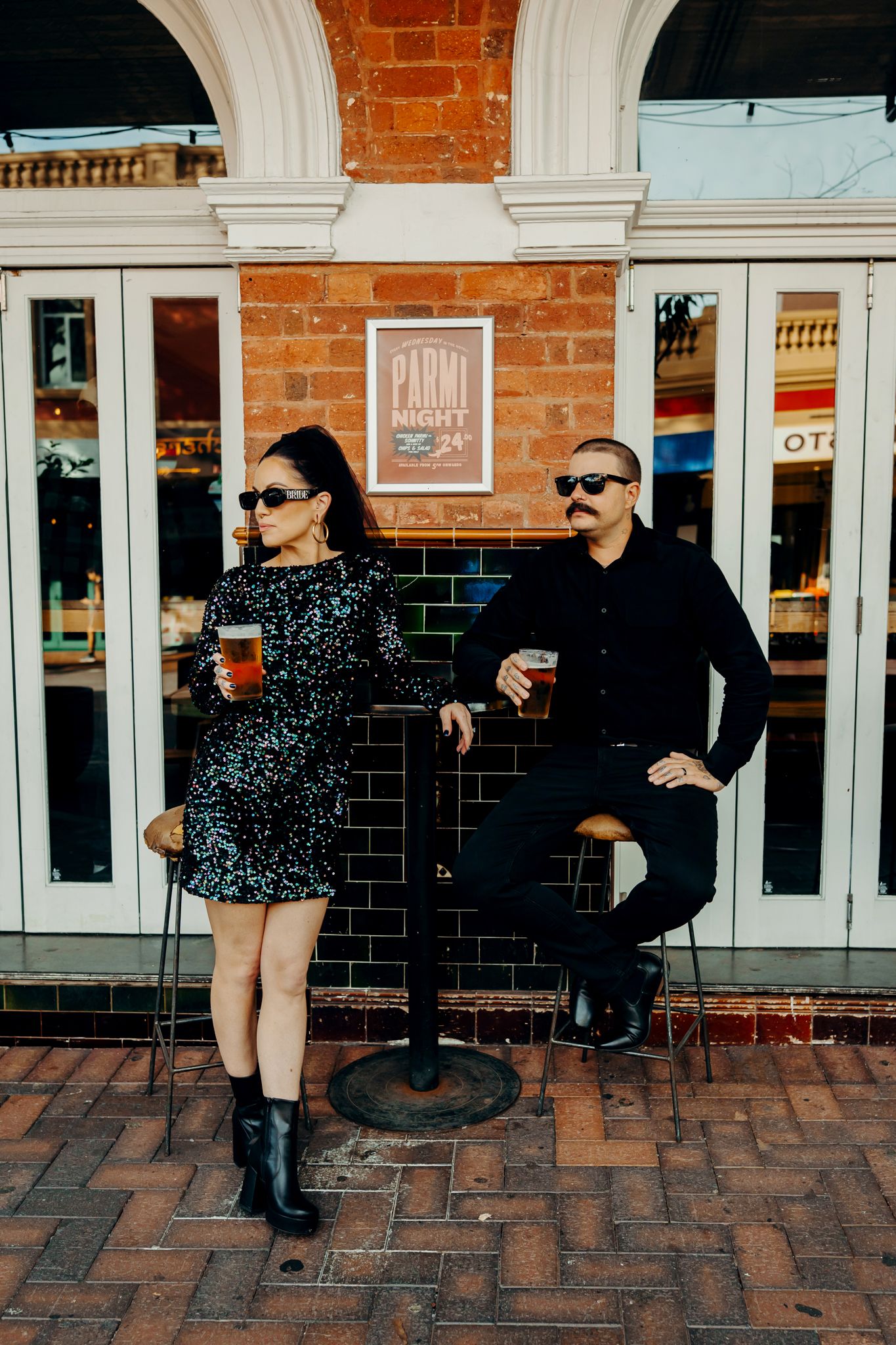 Two people enjoying drinks outside a brick building with arched windows and a Patio sign.