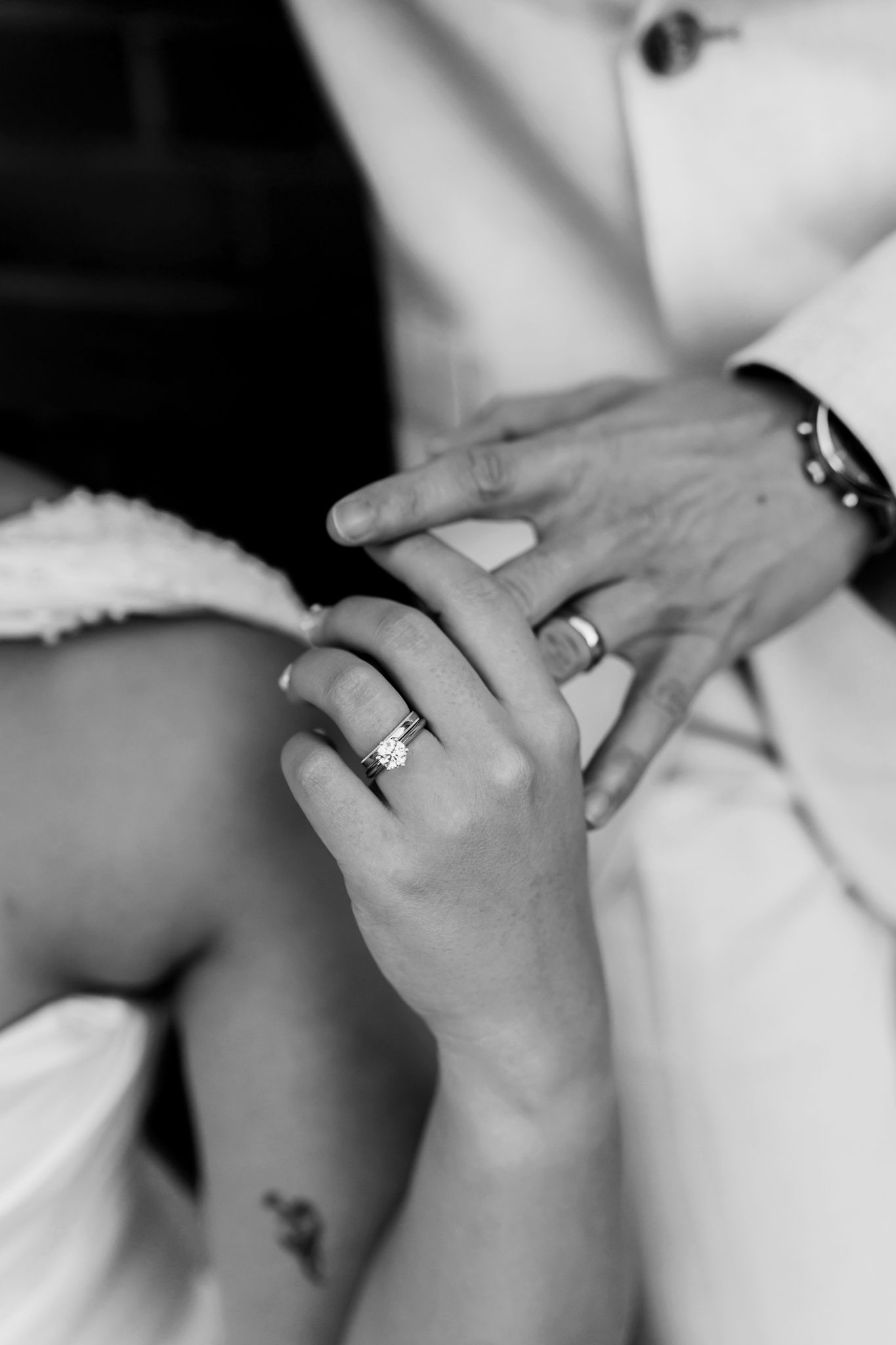 Close-up black and white photo of bride and groom holding hands showing diamond wedding rings.