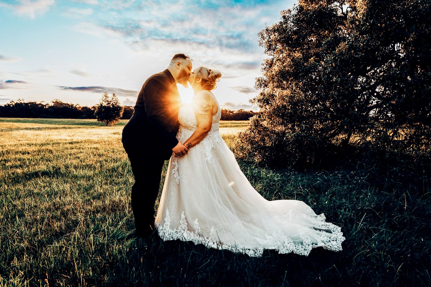 Silhouette of a couple in wedding attire embracing in a field during golden hour sunset.