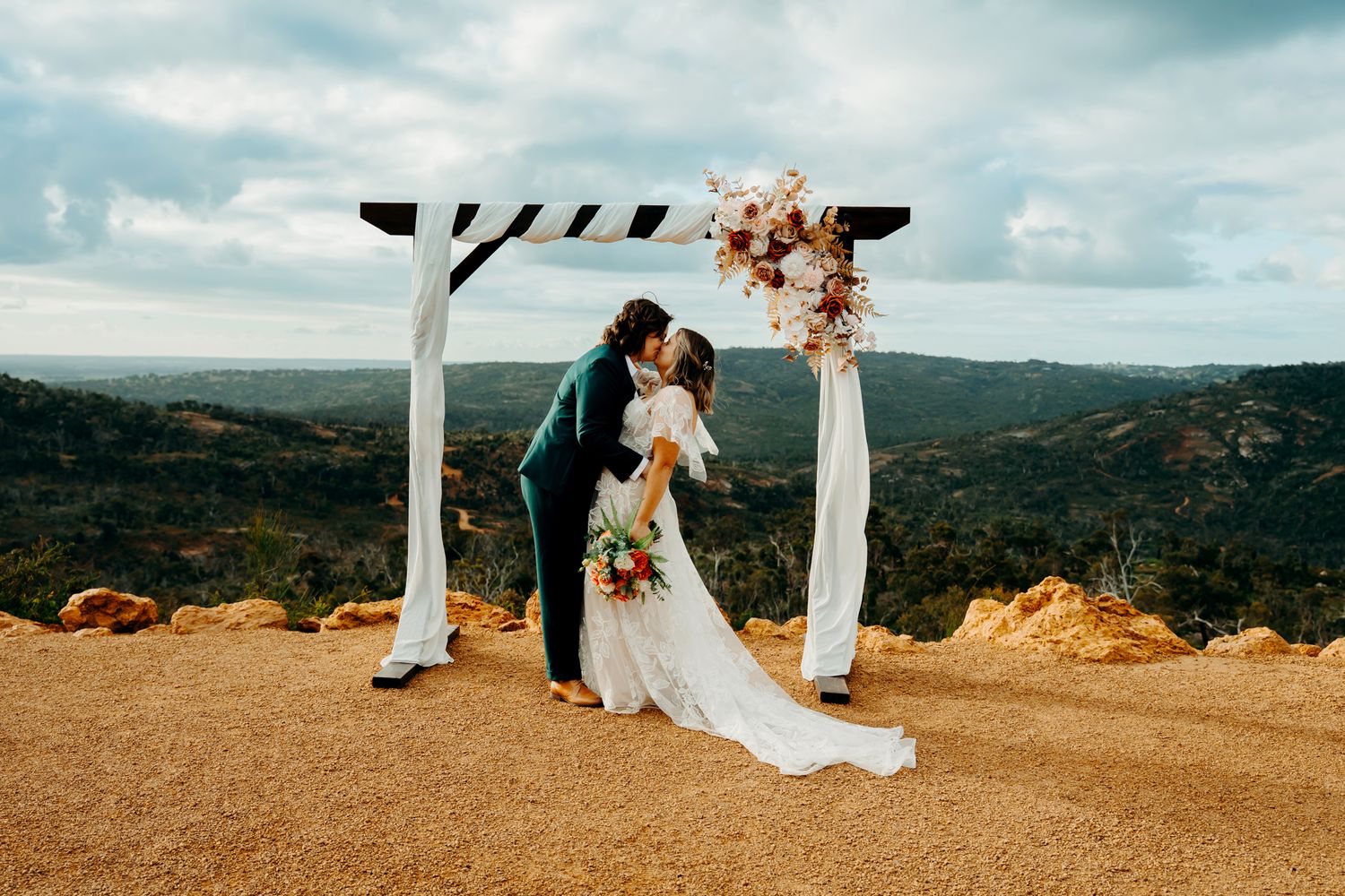 A romantic outdoor wedding ceremony takes place on a scenic mountaintop overlook with white decor and natural landscapes.